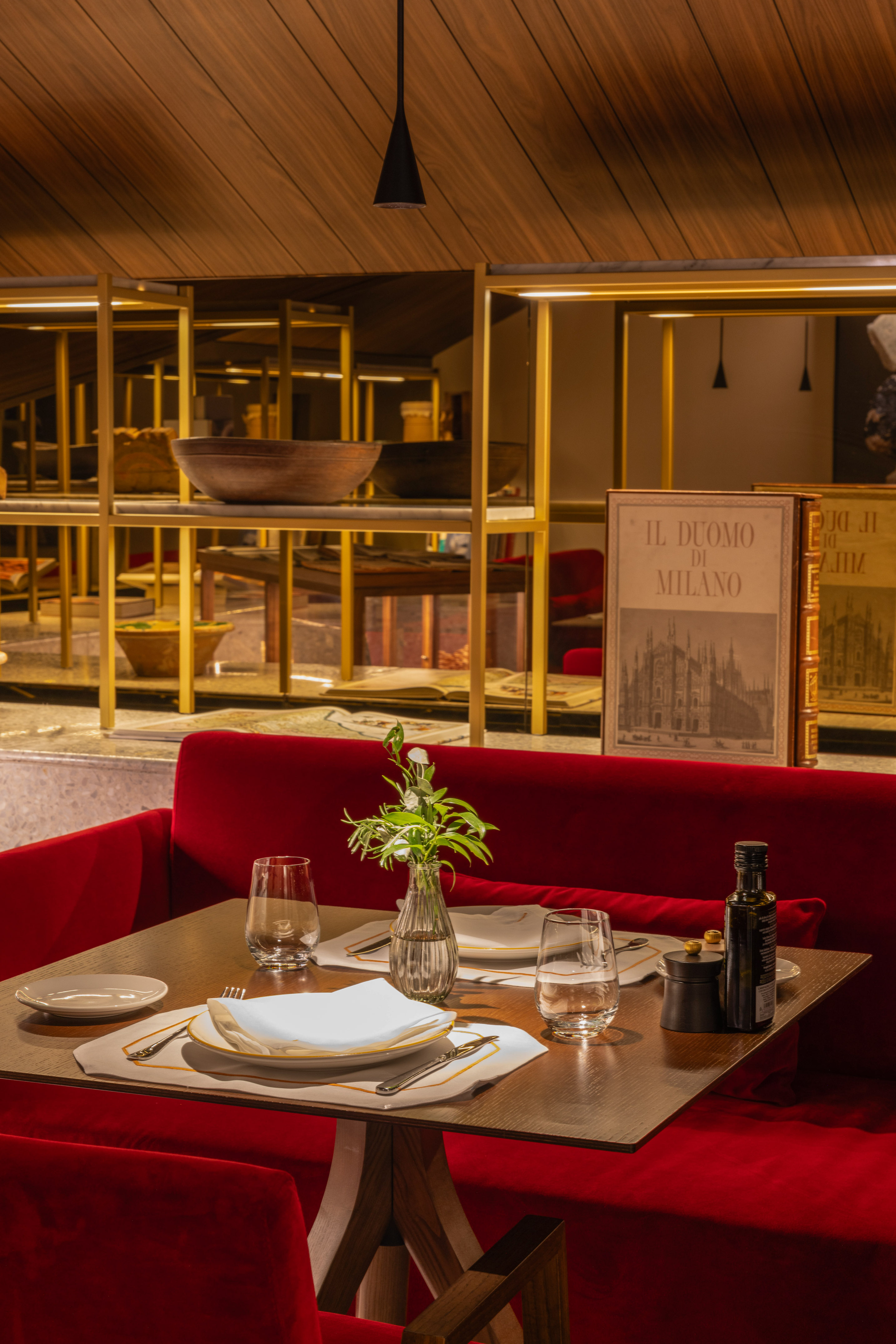 Modern Milanese restaurant with red velvet banquette, set dining table.