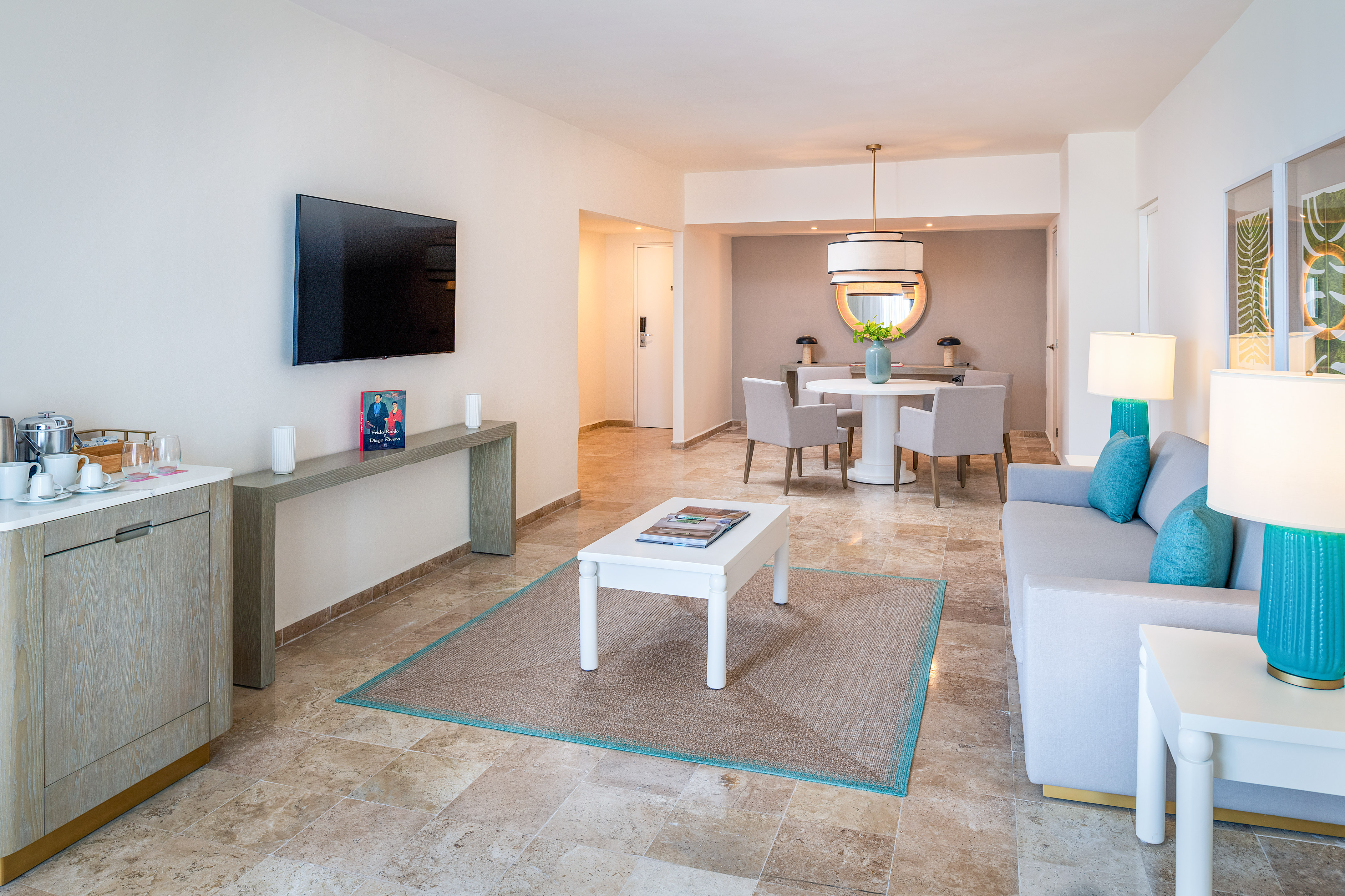 Modern open concept living room and dining area with light decor and travertine floor.