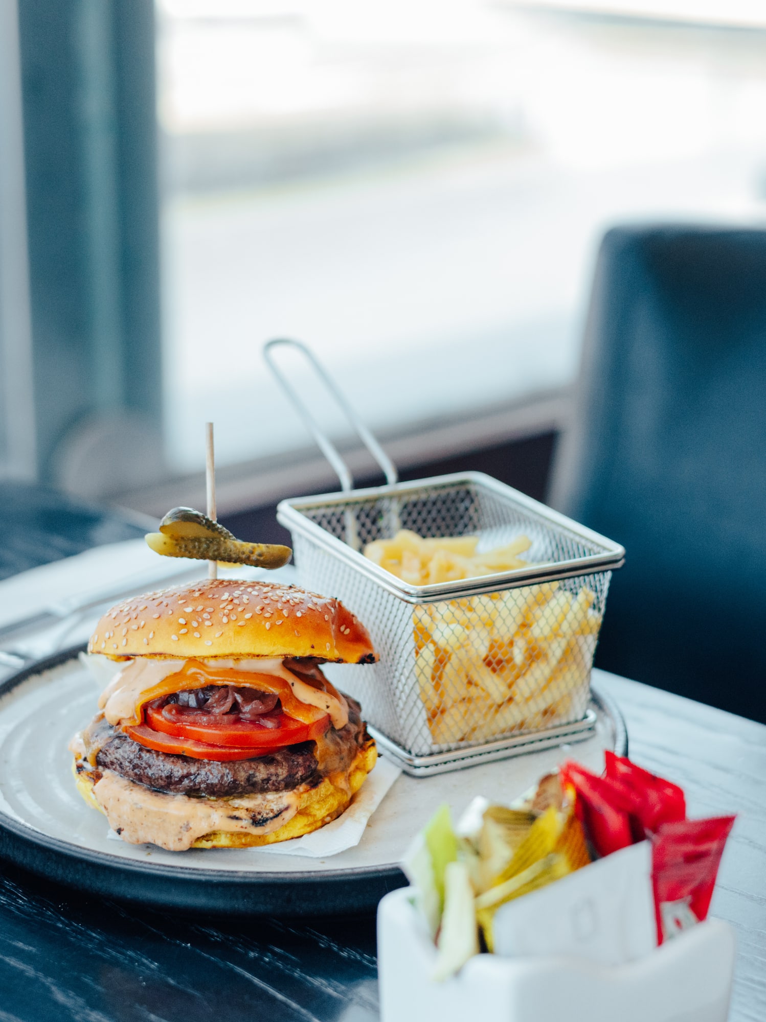 Gourmet burger with french fries, water bottle, and condiments on a table.
