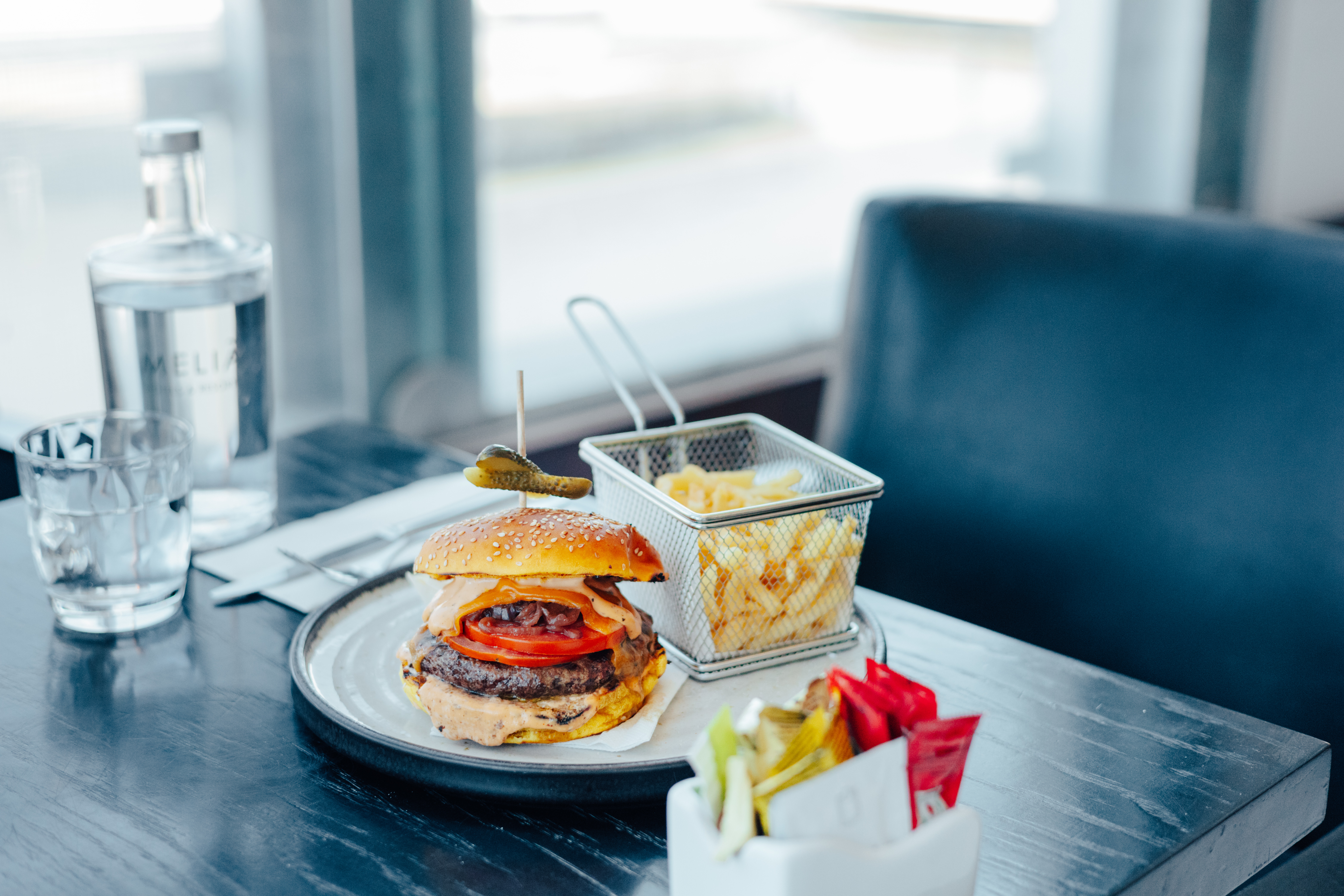 Gourmet burger with french fries, water bottle, and condiments on a table.