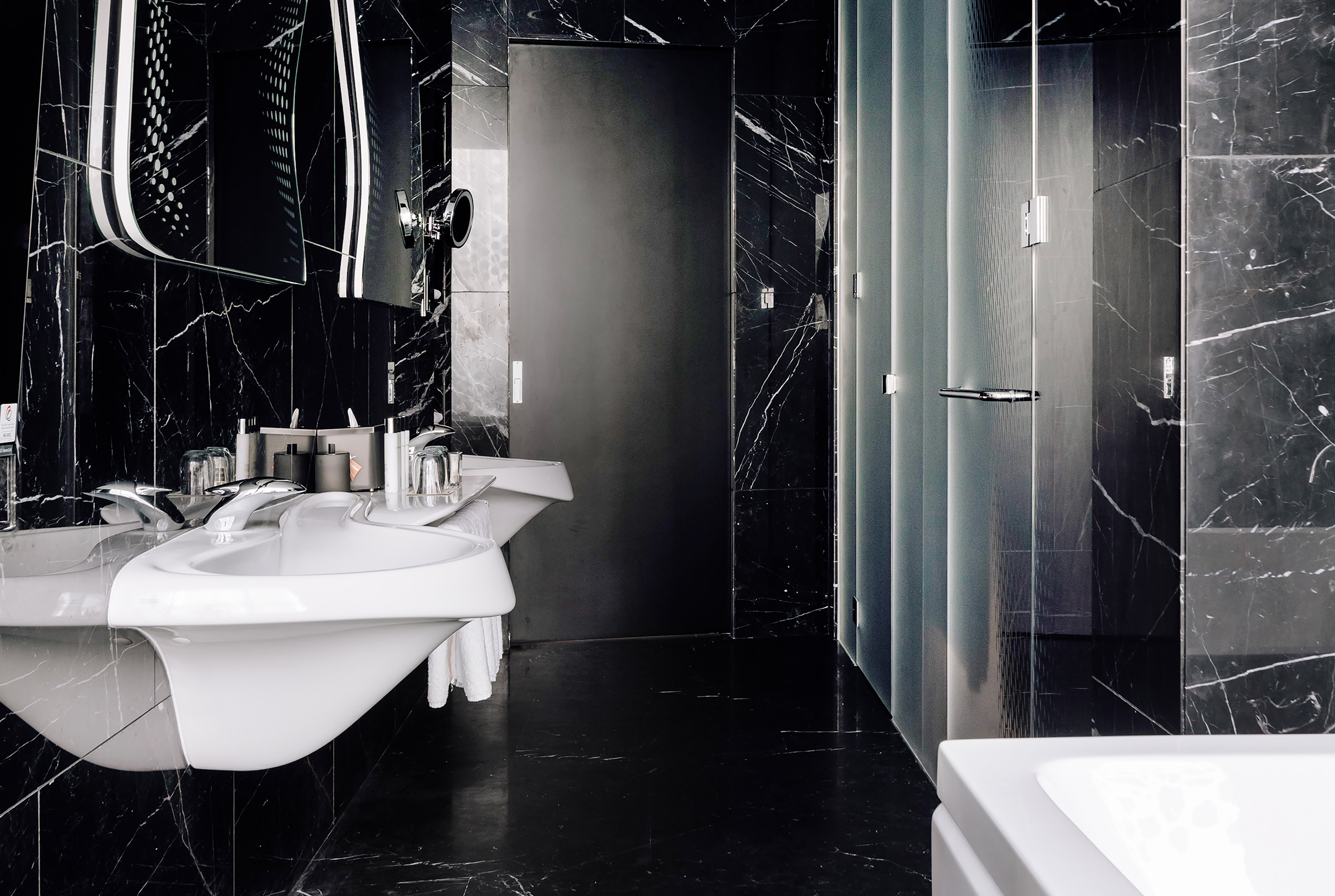 Sleek black marble bathroom with modern double vanity, illuminated mirror, and glass shower.