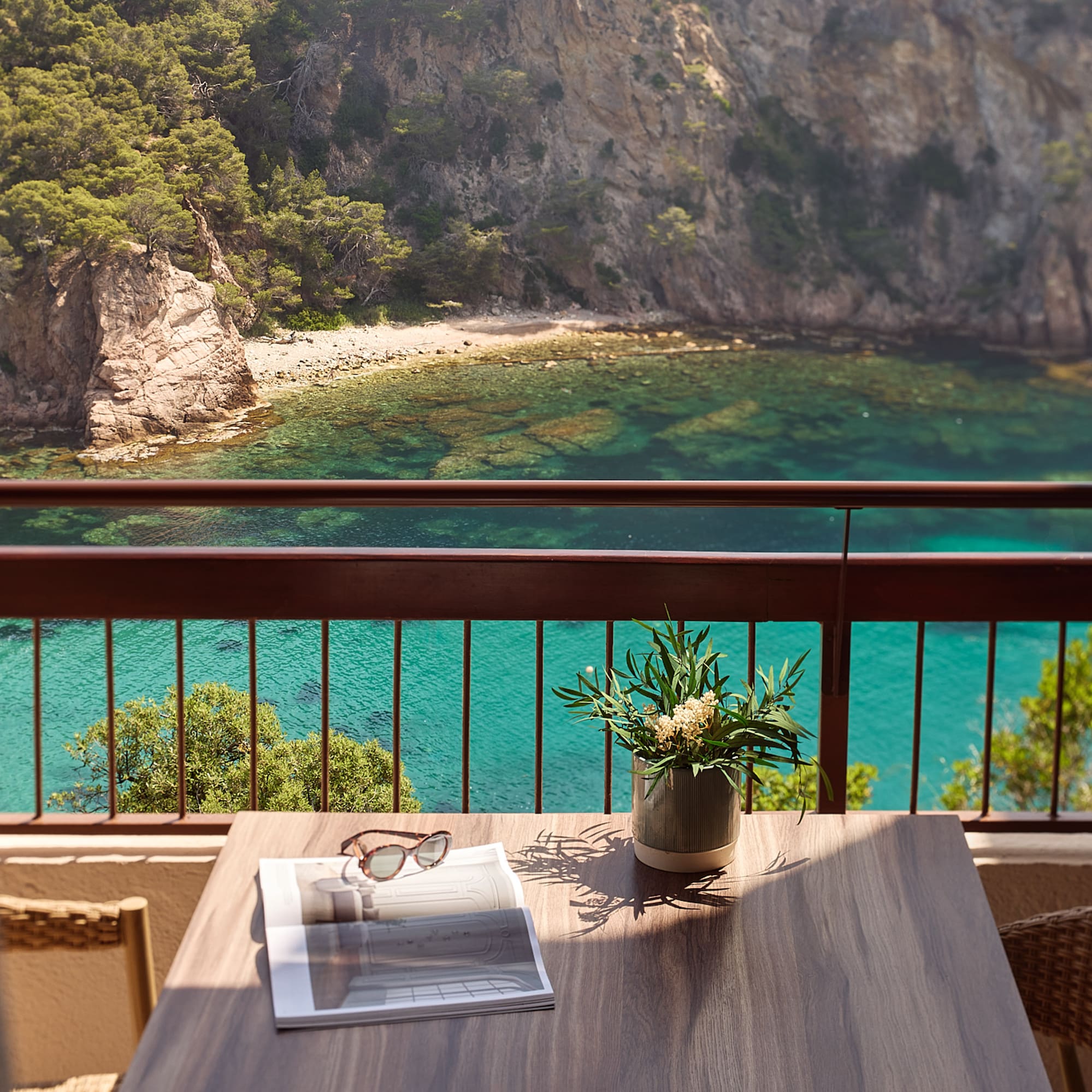 a table with a vase of sunglasses and a vase of flowers on a balcony overlooking a body of water