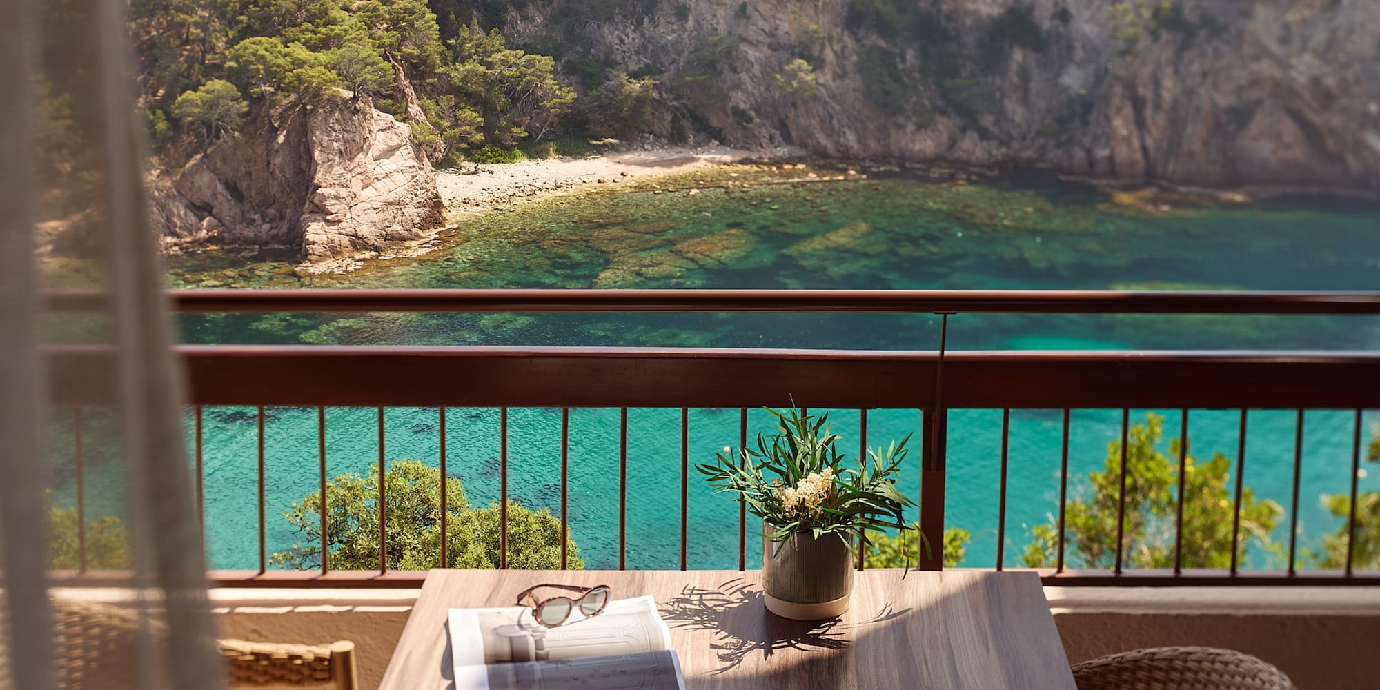 a table with a vase of sunglasses and a vase of flowers on a balcony overlooking a body of water