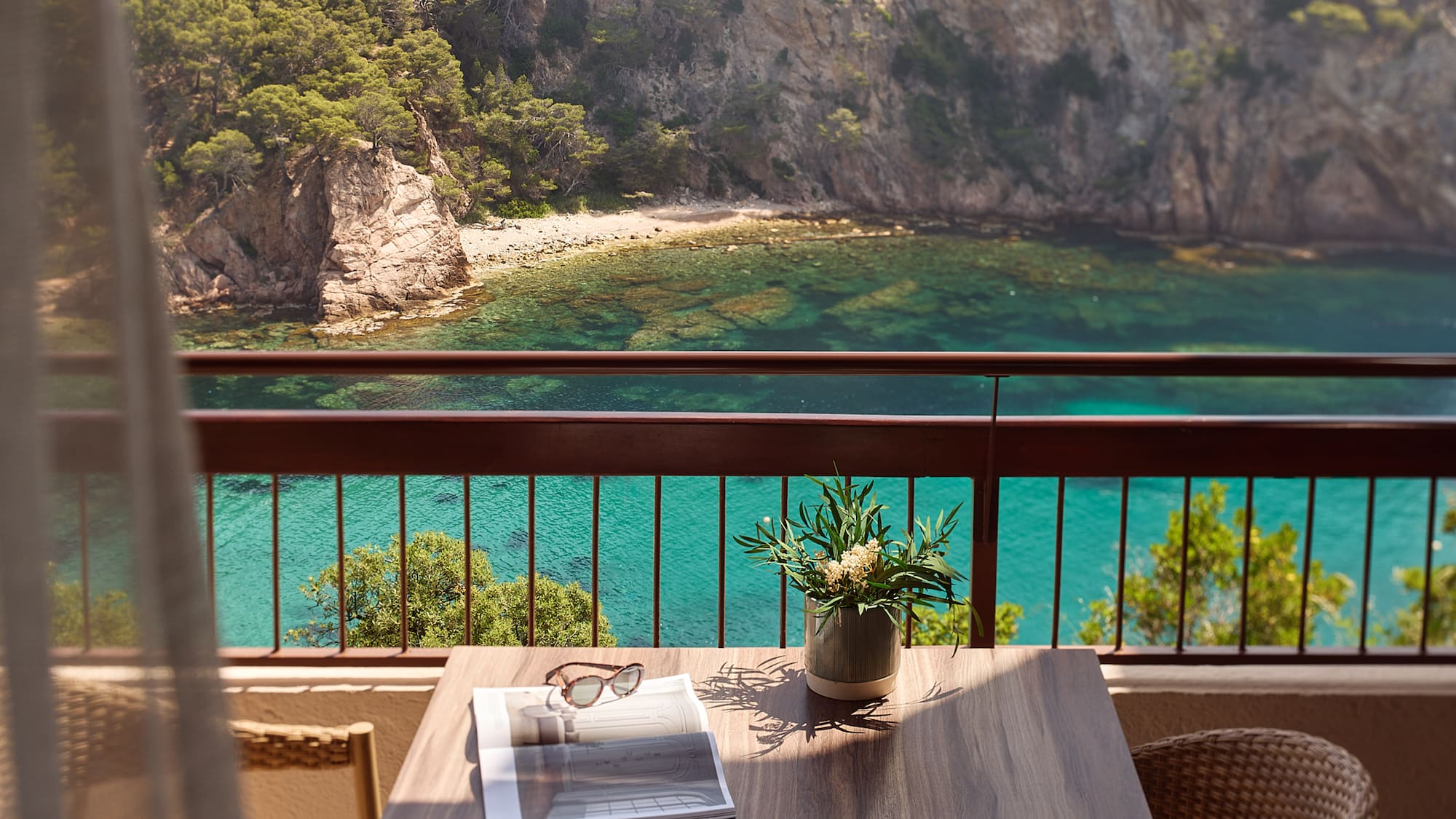 a table with a vase of sunglasses and a vase of flowers on a balcony overlooking a body of water
