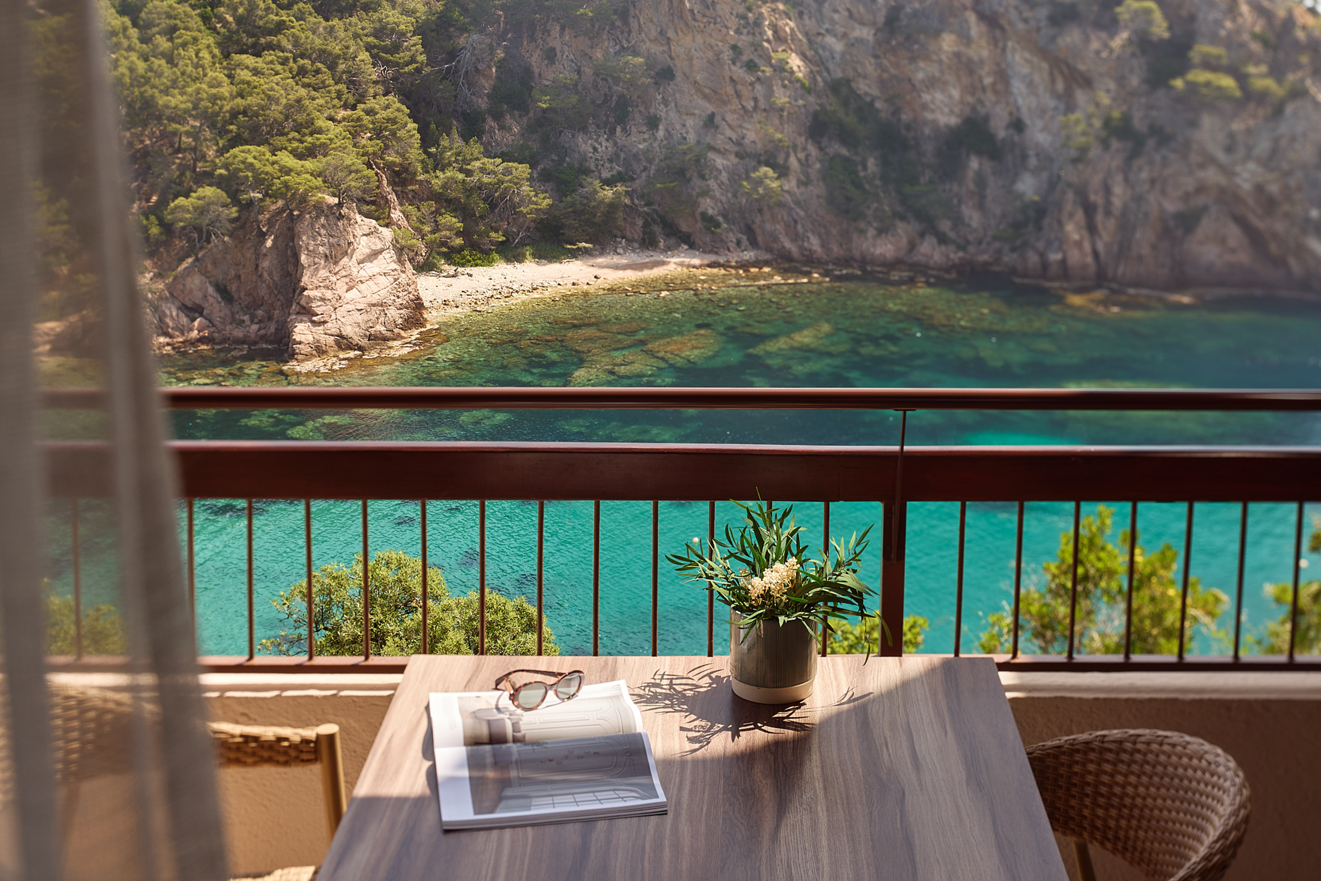 a table with a vase of sunglasses and a vase of flowers on a balcony overlooking a body of water