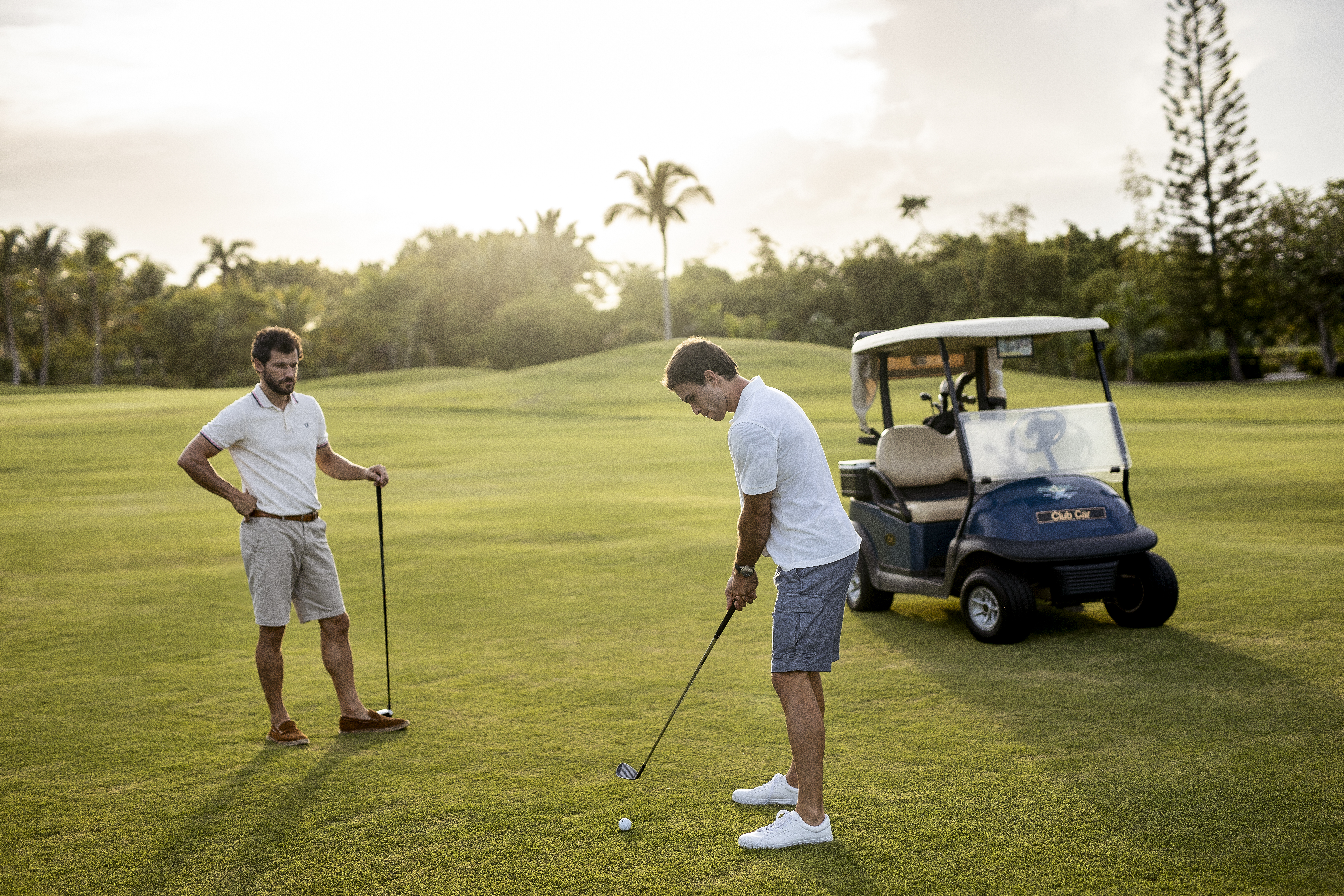a man holding a golf club and another man standing on a golf cart
