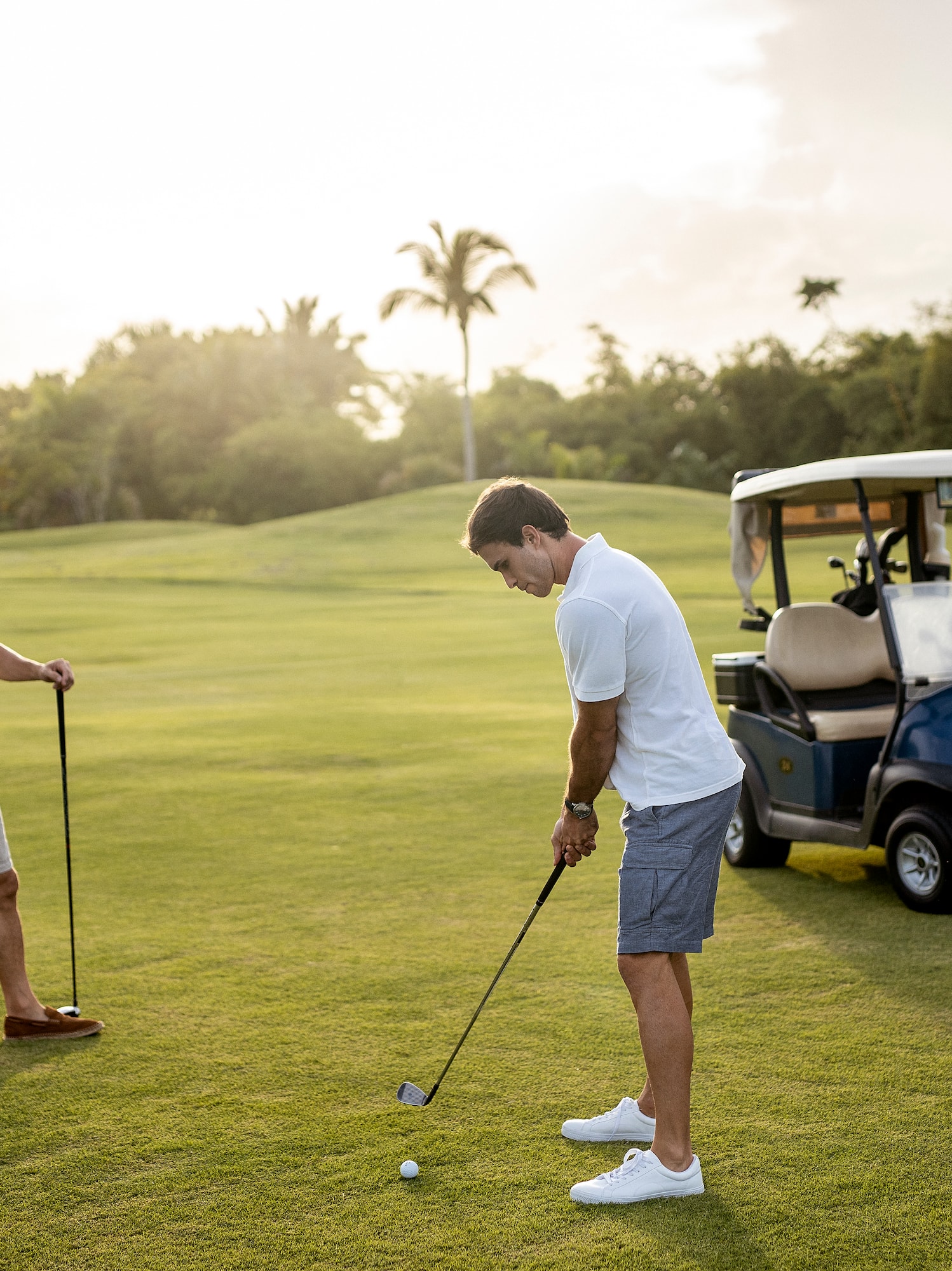 a man holding a golf club and another man standing on a golf cart