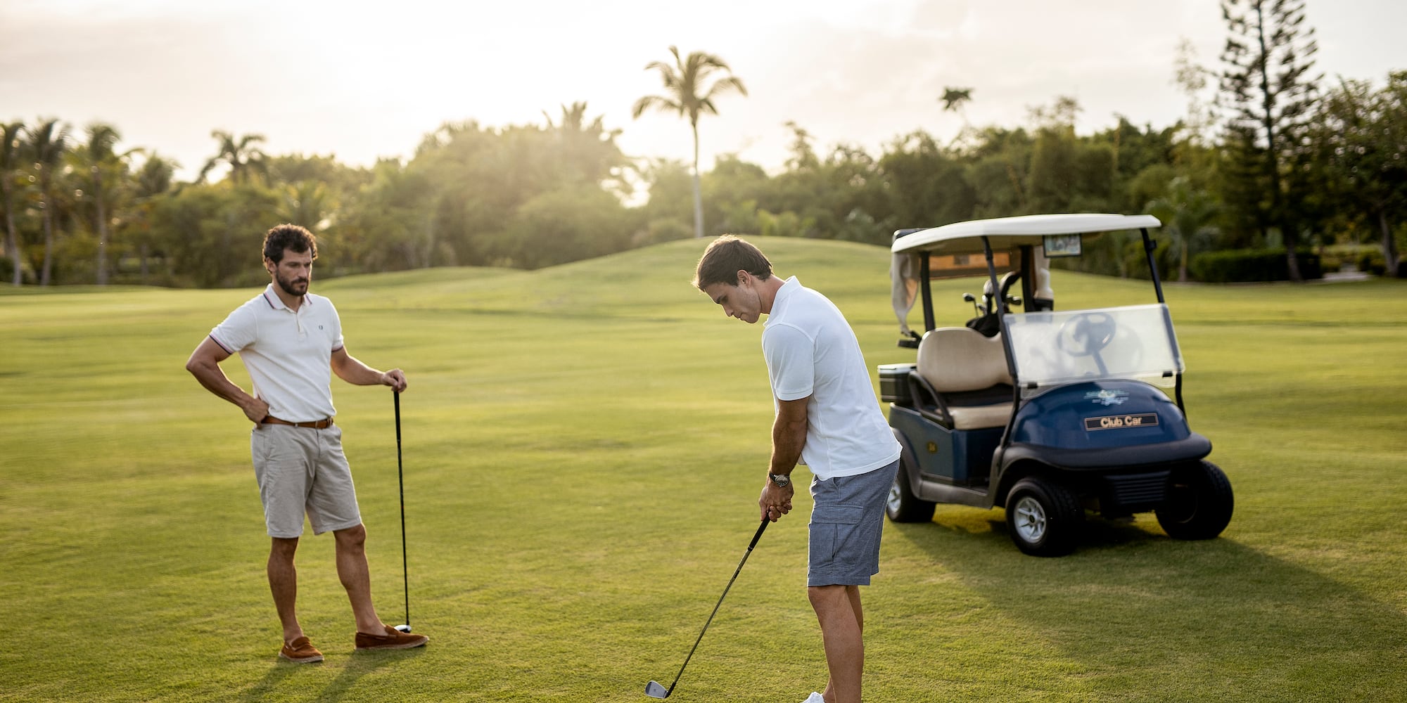 a man holding a golf club and another man standing on a golf cart