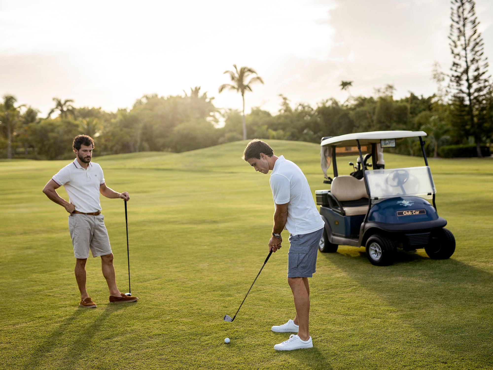 a man holding a golf club and another man standing on a golf cart
