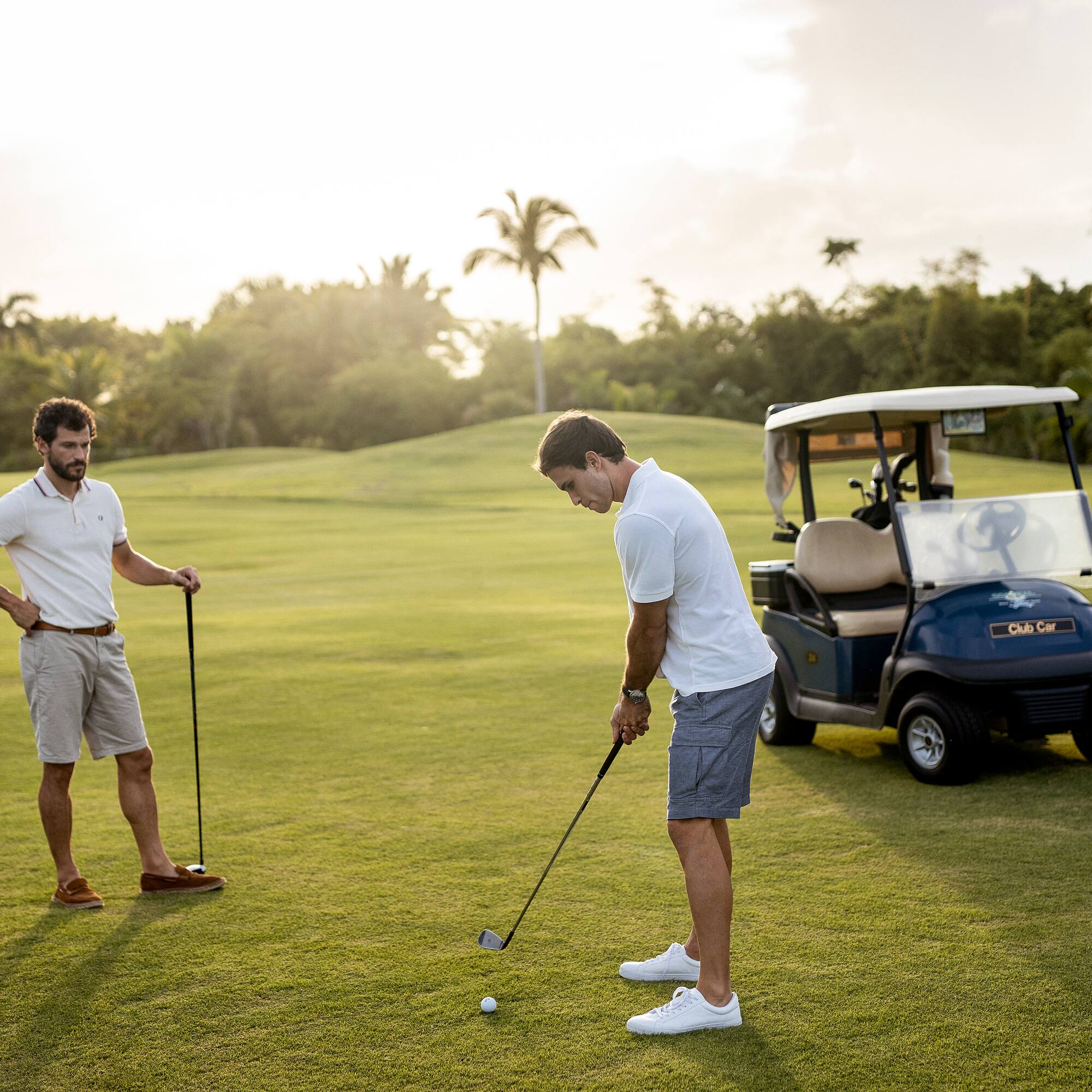 a man holding a golf club and another man standing on a golf cart