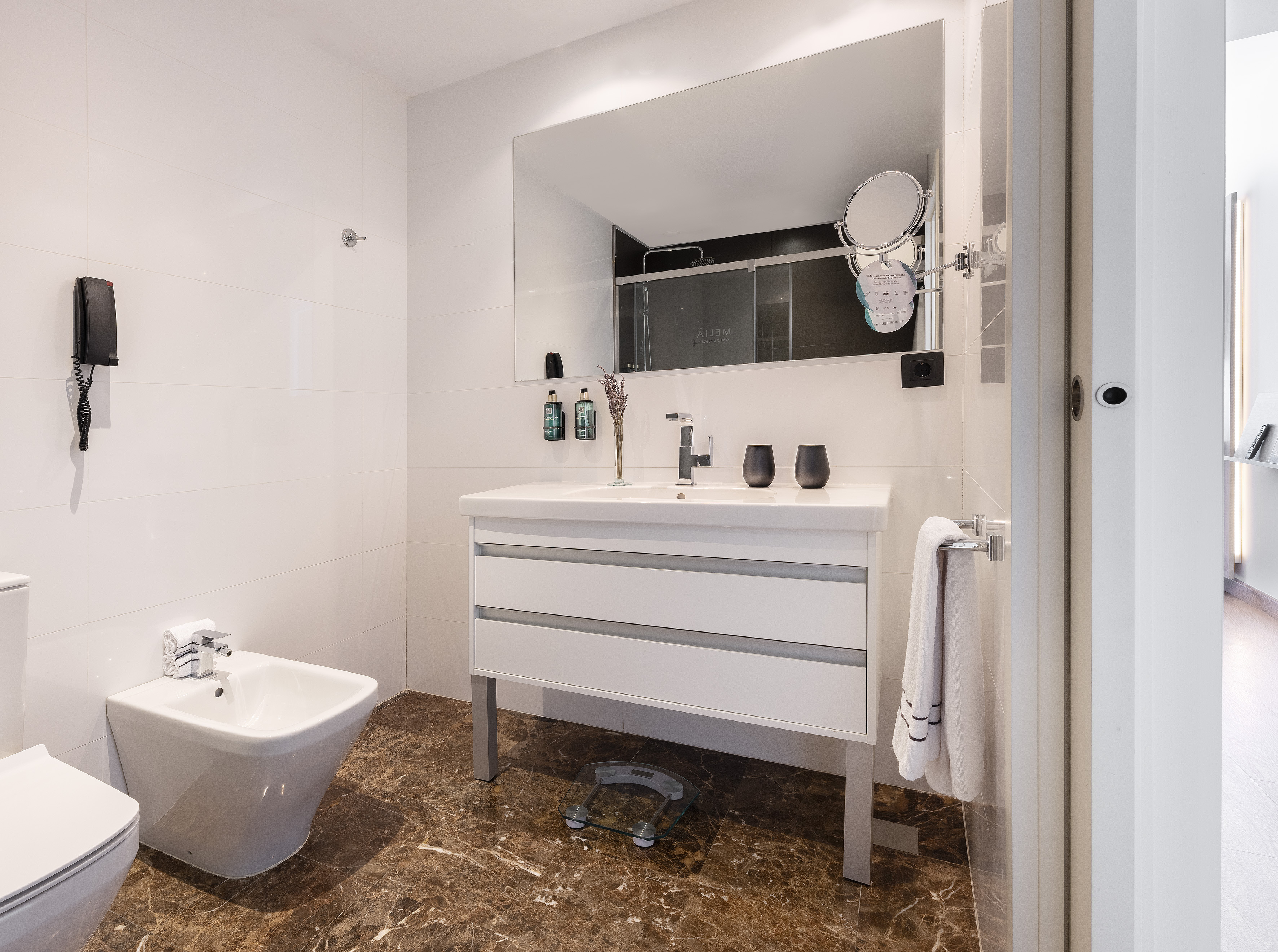 Modern white bathroom with vanity, large mirror, bidet, toilet, and marble floor.