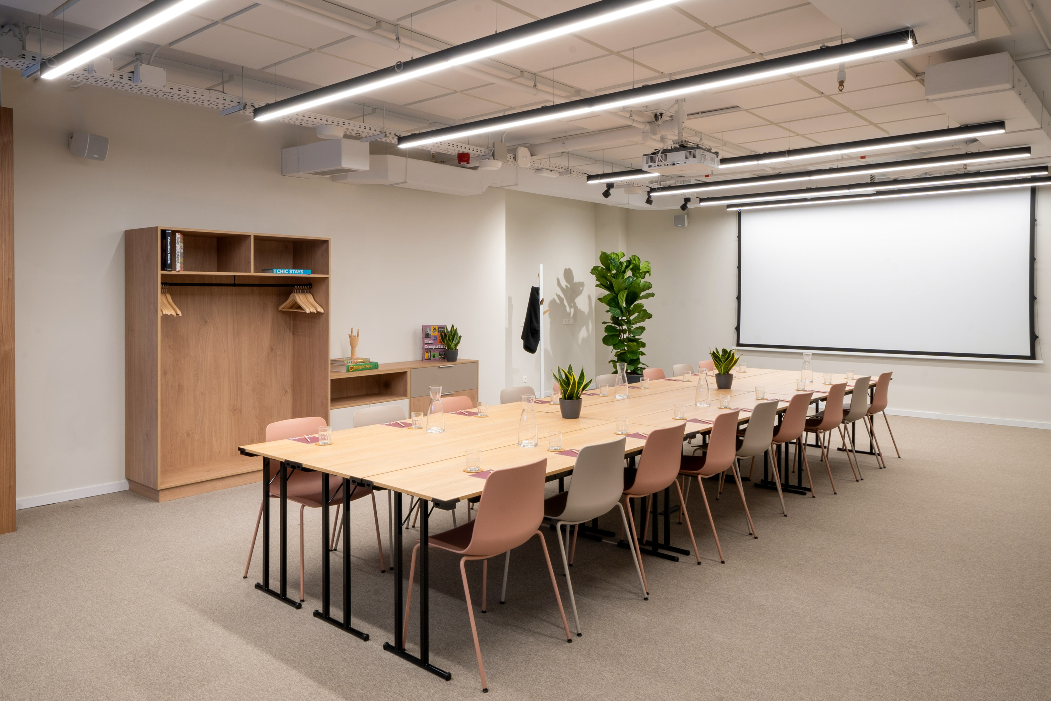 Modern conference room with large screen, long table, and pink chairs.