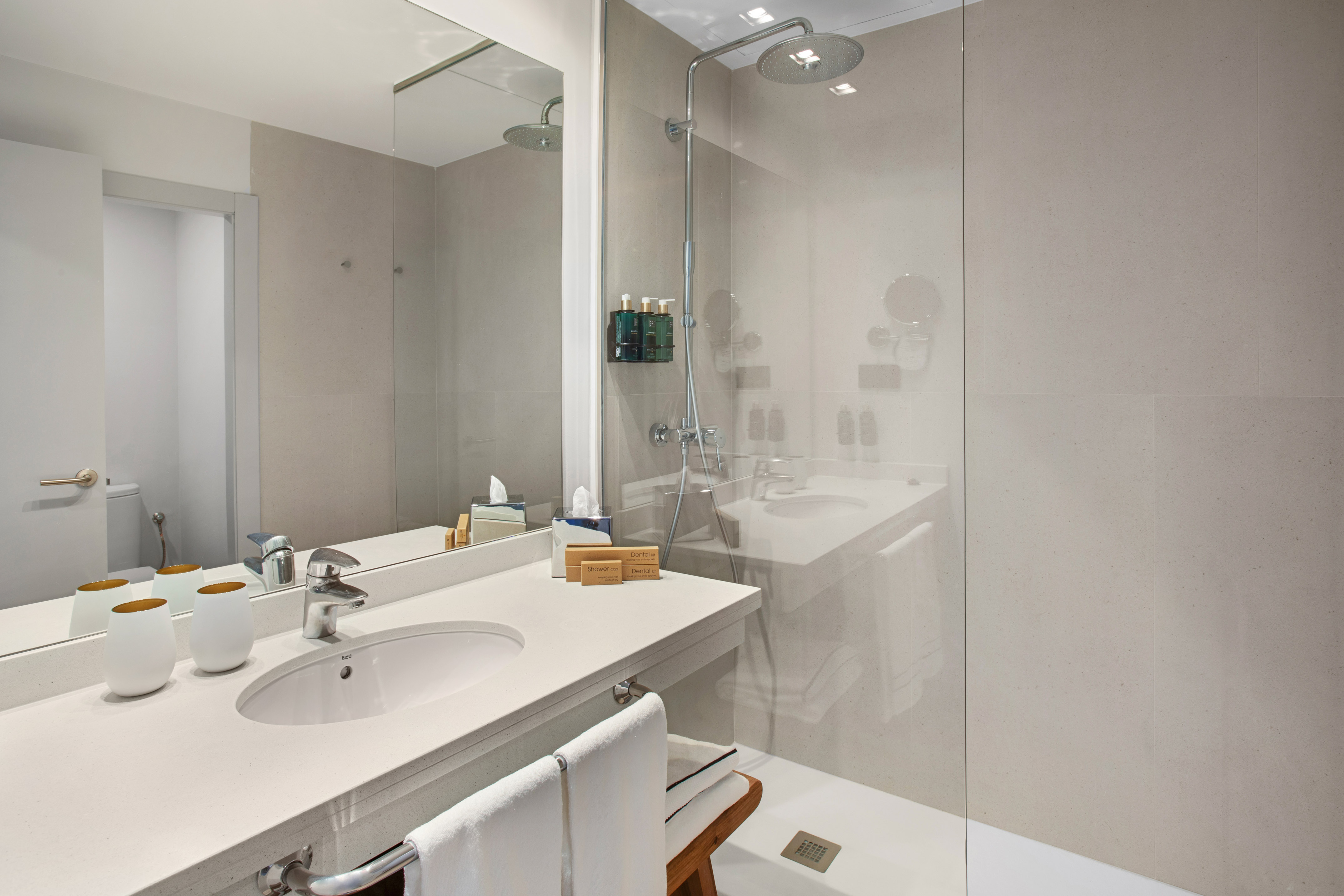 Modern hotel bathroom with vanity, sink, mirror, and walk-in shower.