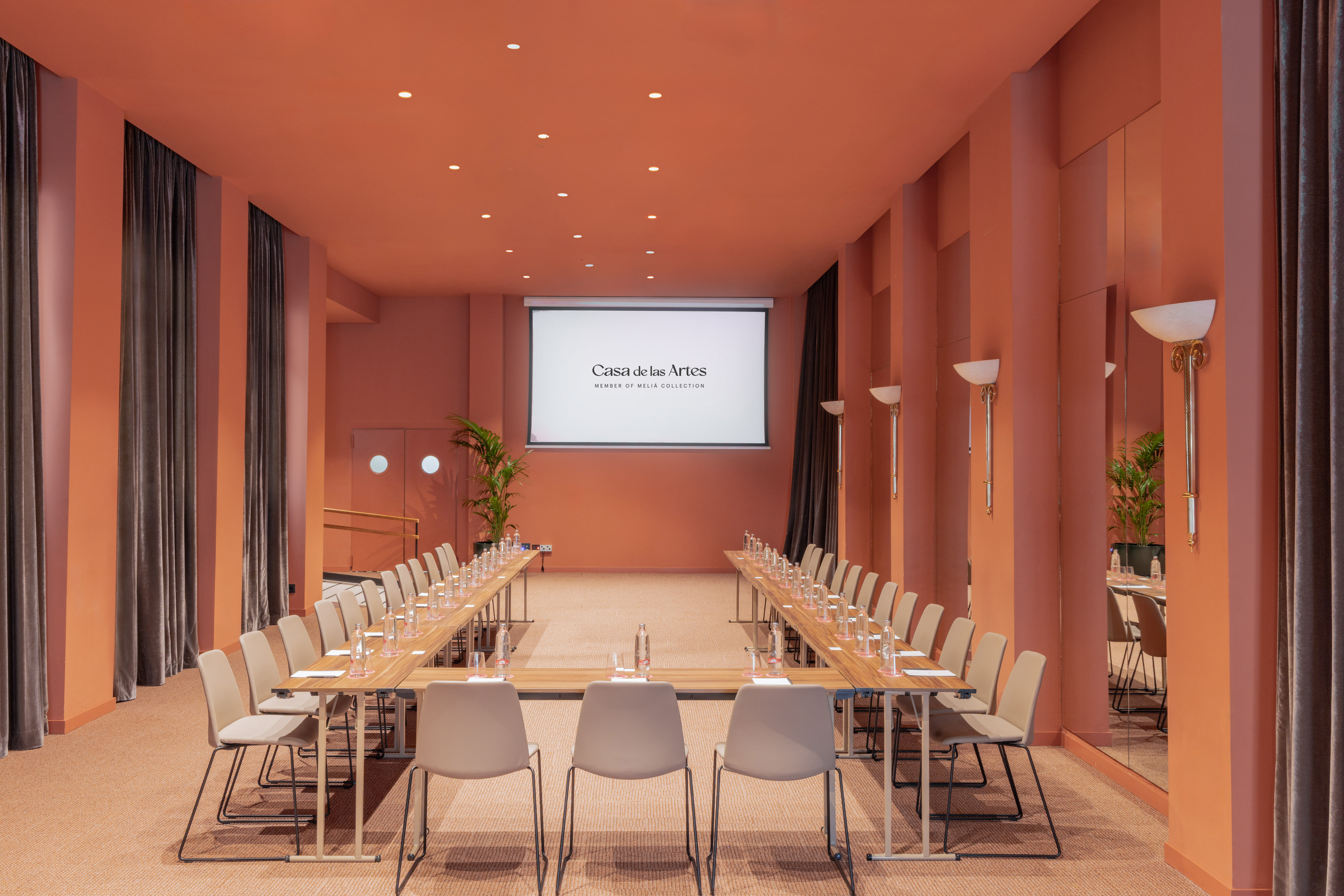 Casa de las Artes meeting room with U-shape setup, screen, and terracotta walls.
