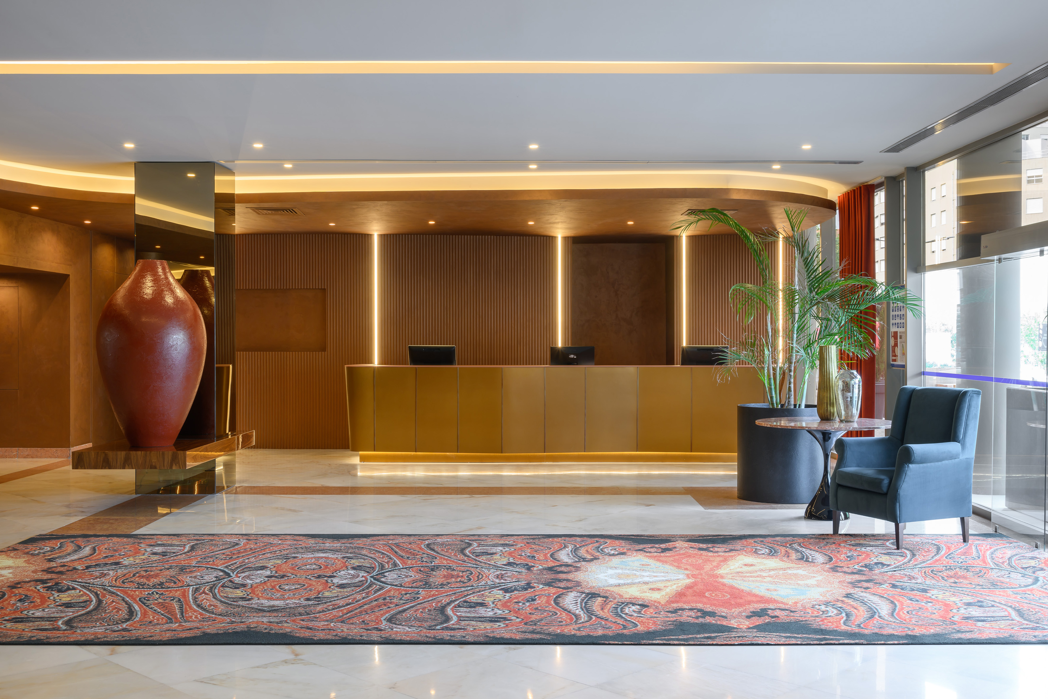 Modern hotel lobby with golden reception desk, ornate carpet, and warm lighting.