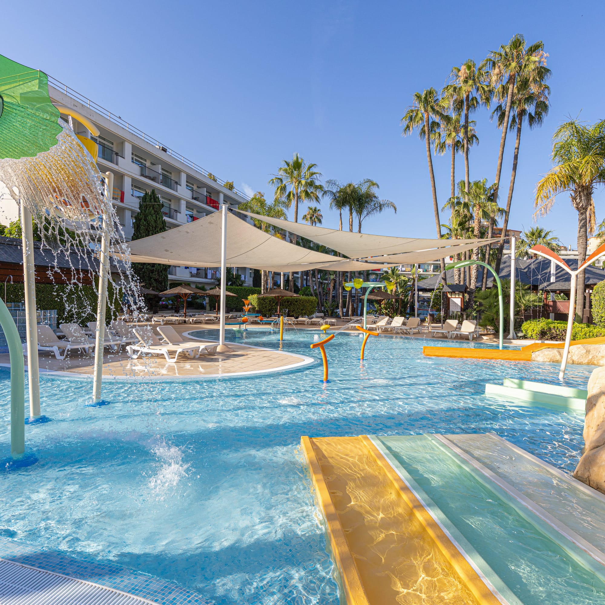 Family hotel water park with kids' splash zone, slides, and palm trees.