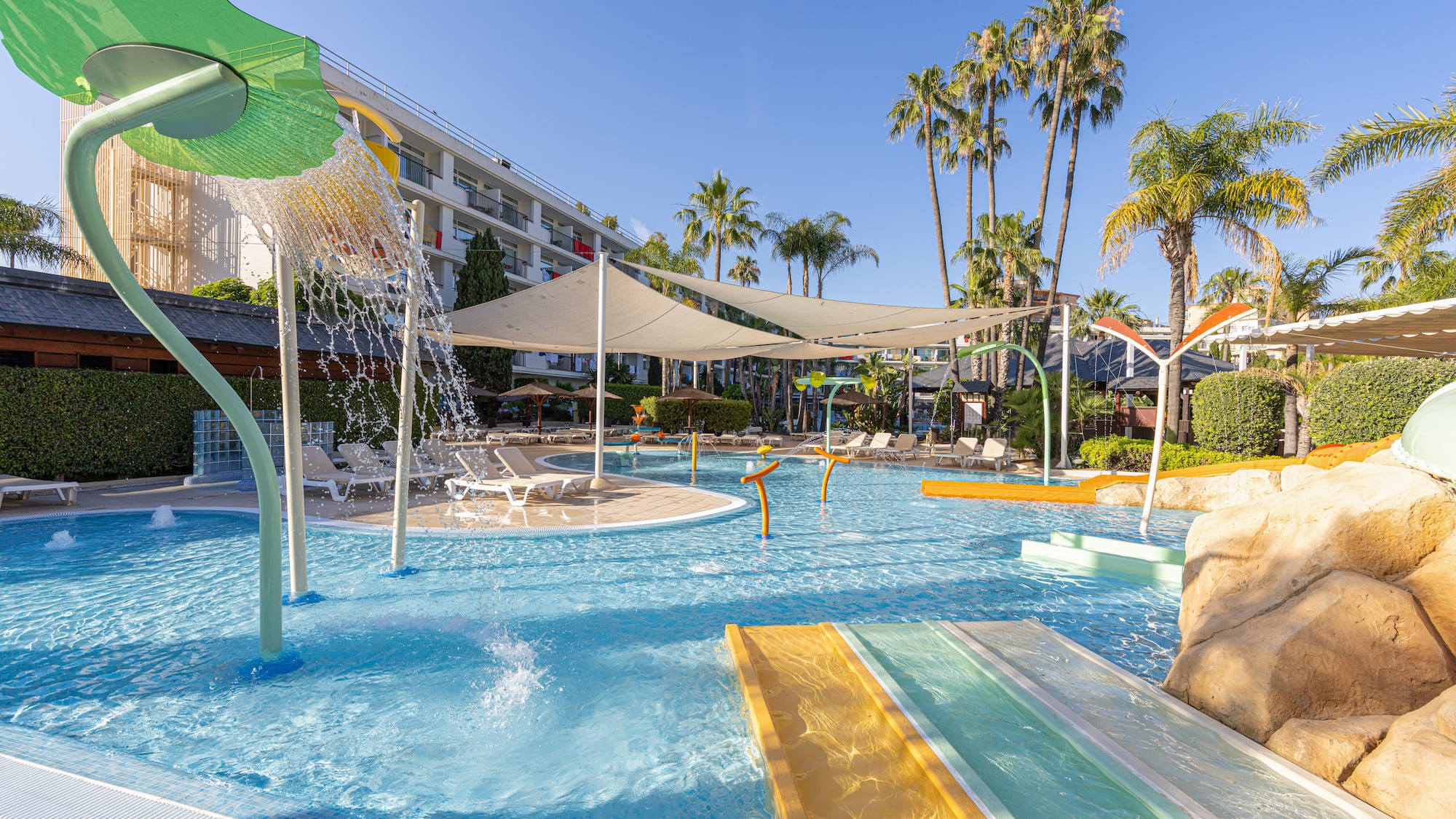 Family hotel water park with kids' splash zone, slides, and palm trees.