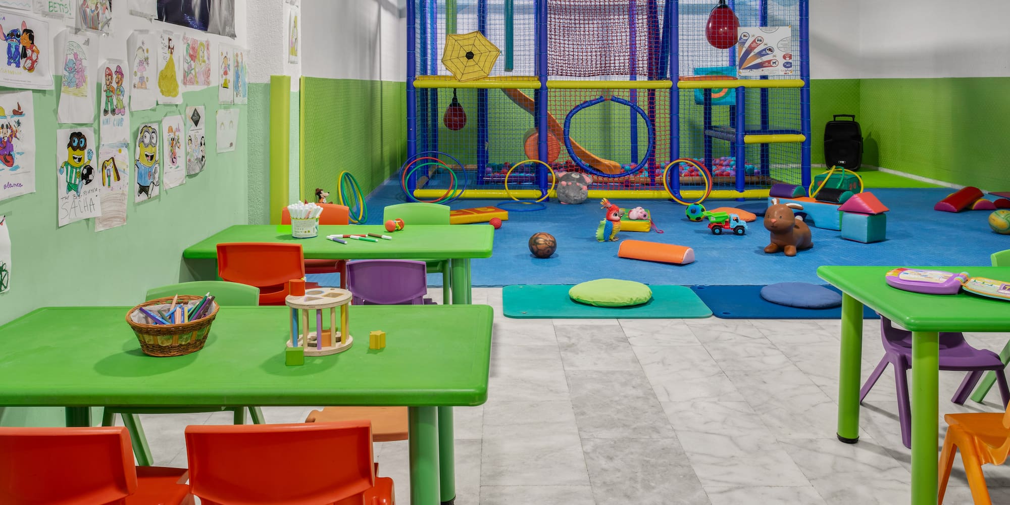 Colorful indoor kids' play area with soft play structure and craft tables.