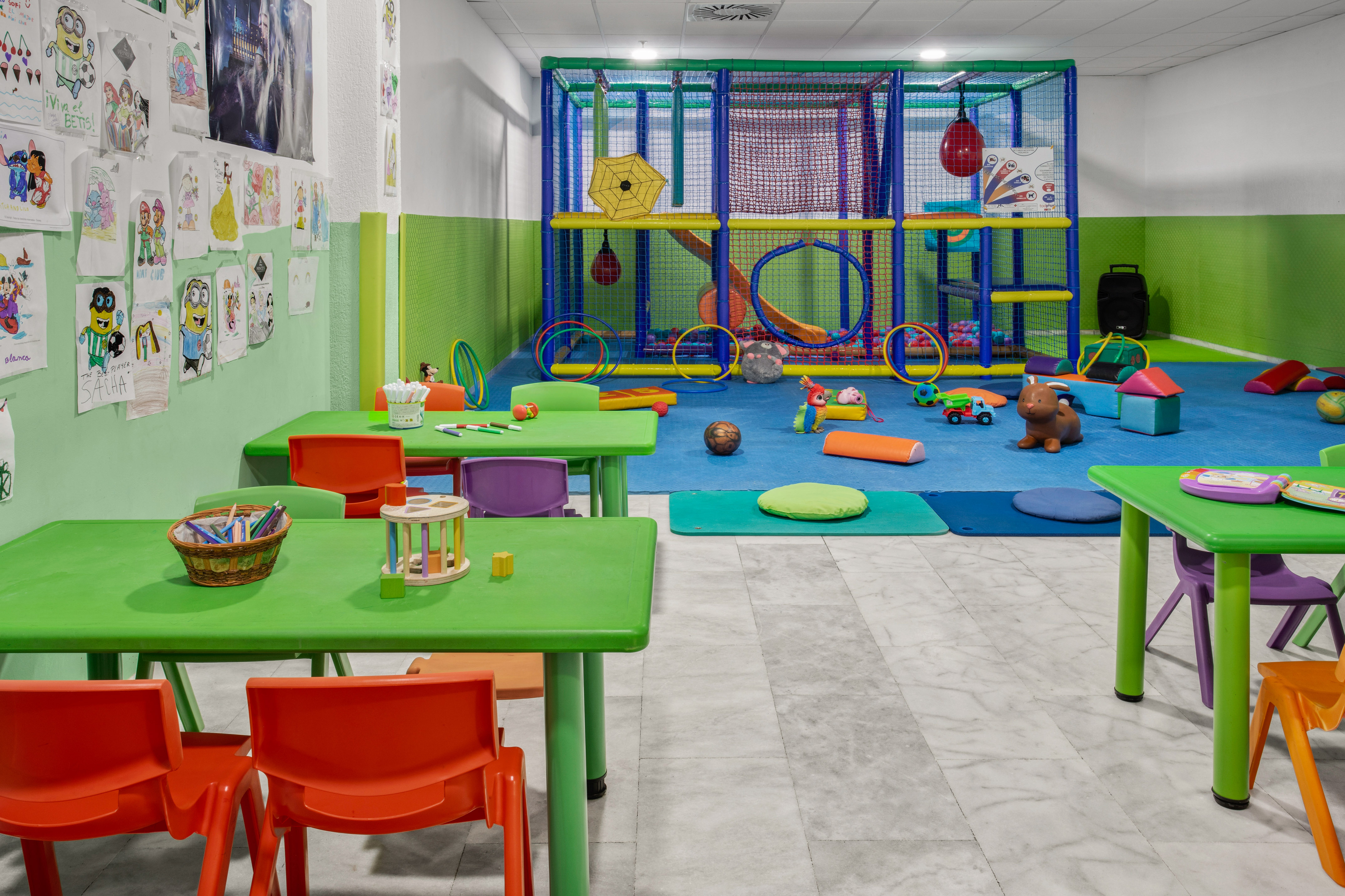 Colorful indoor kids' play area with soft play structure and craft tables.