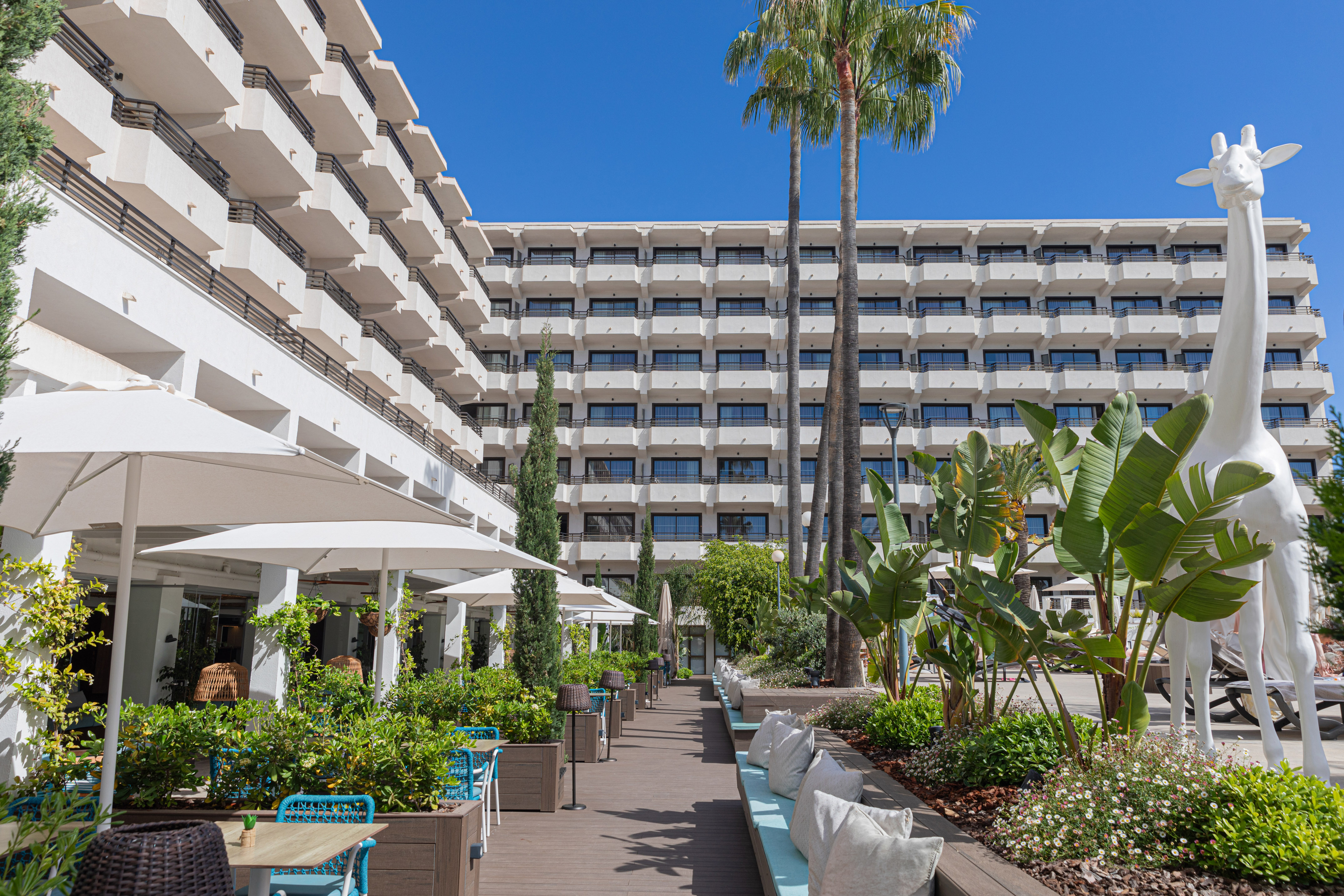 Resort hotel exterior with lush garden, outdoor cafe, and white giraffe statue.