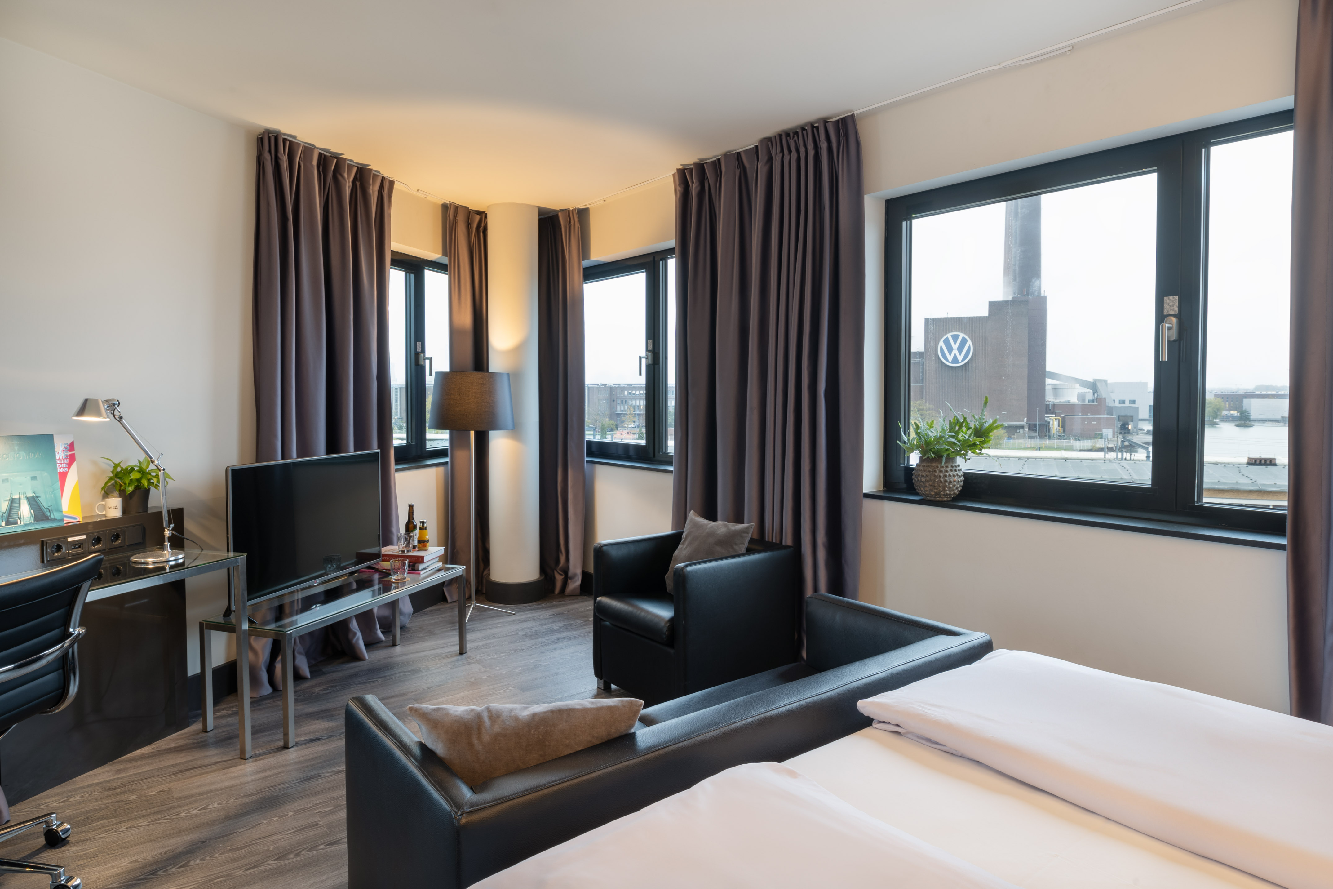 Modern hotel room with beds, desk, and industrial Volkswagen view.