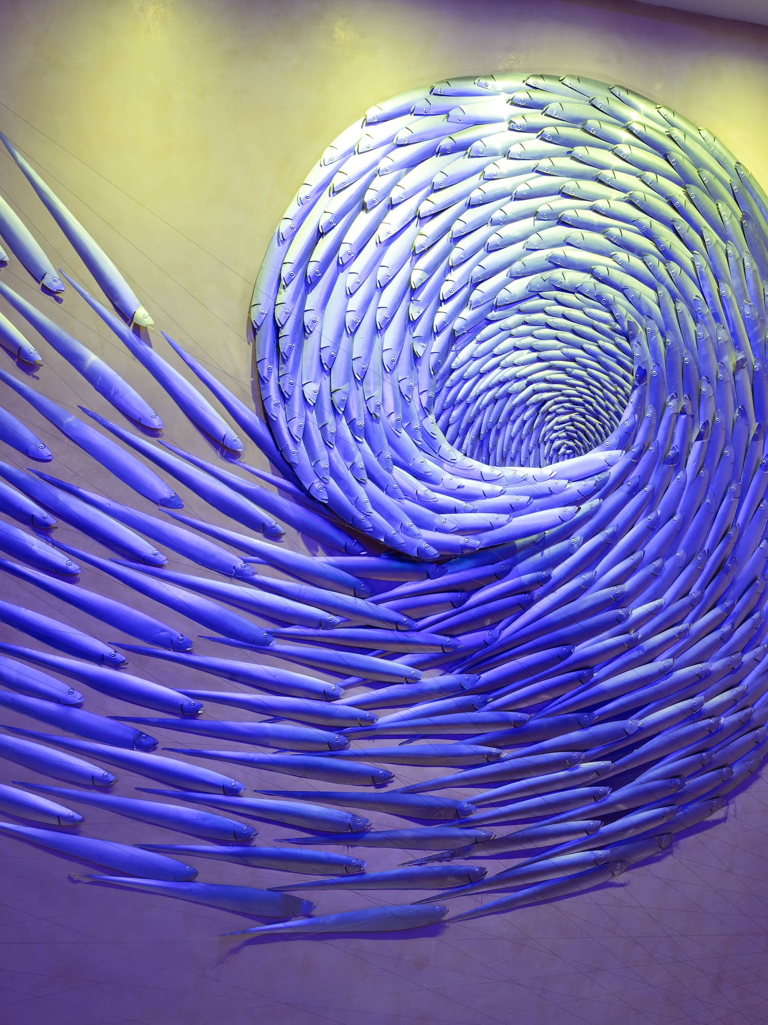 Blue fish spiral wall sculpture with dramatic blue and yellow lighting.