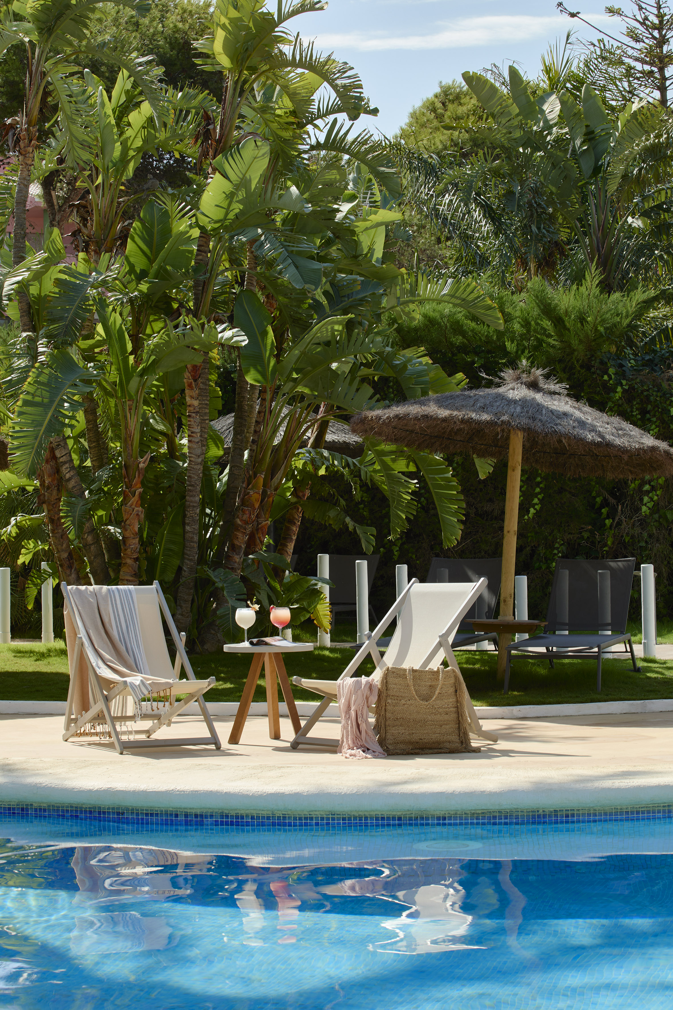 Relaxing tropical pool scene with lounge chairs, cocktails, and palm trees.