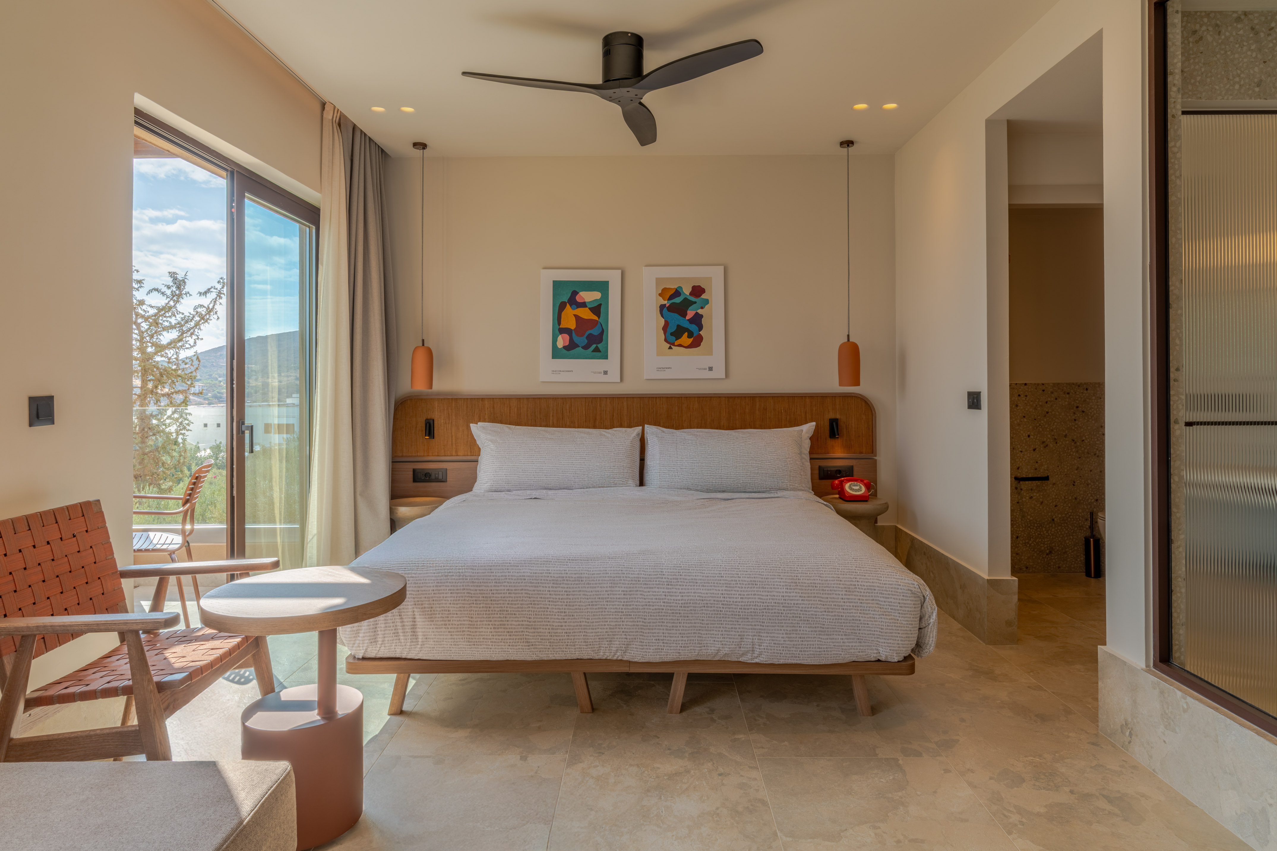 Contemporary hotel bedroom with balcony sea view, large bed, and ceiling fan.