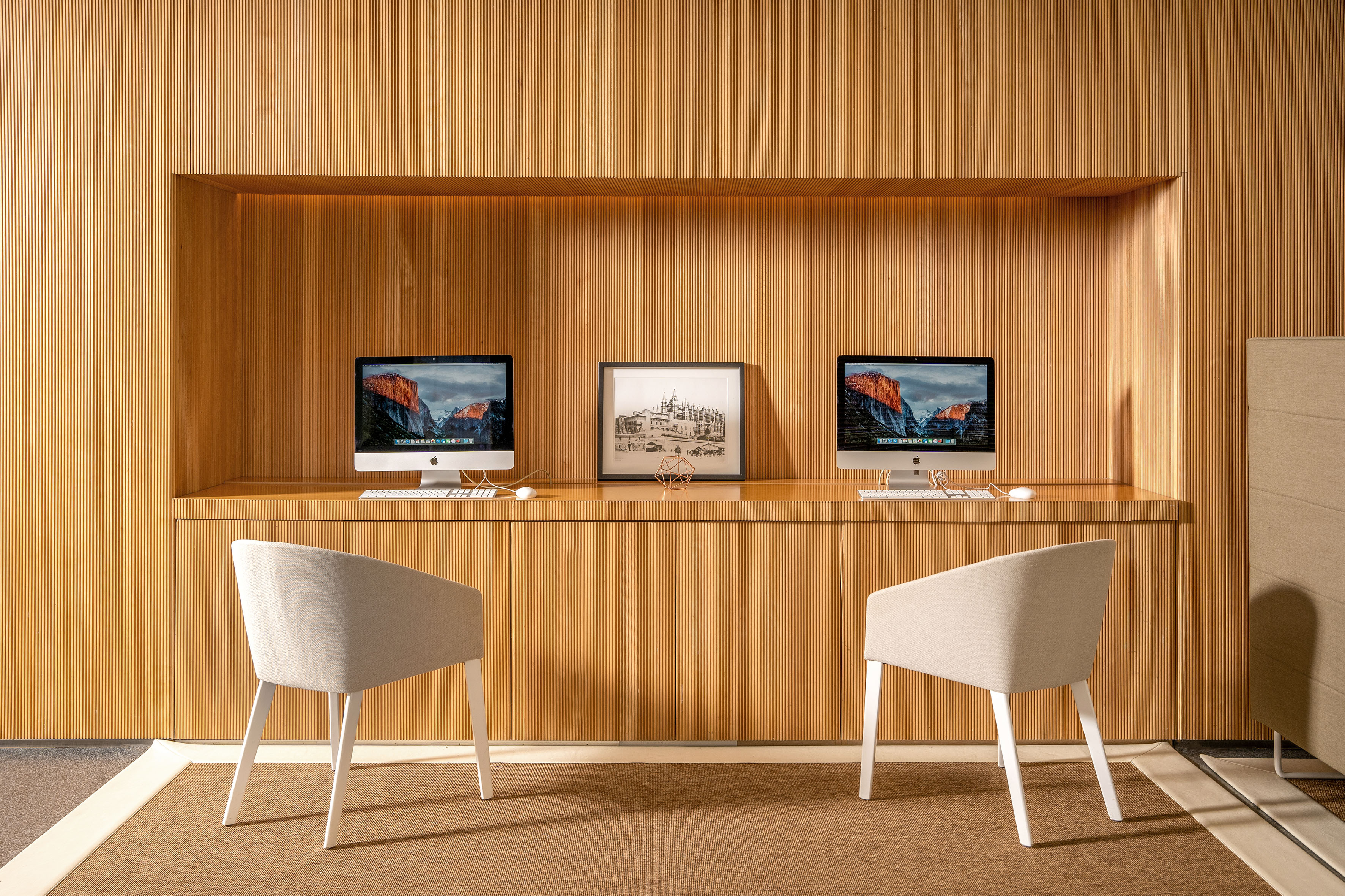 Modern wooden ribbed panel business center with two iMacs and comfortable chairs.