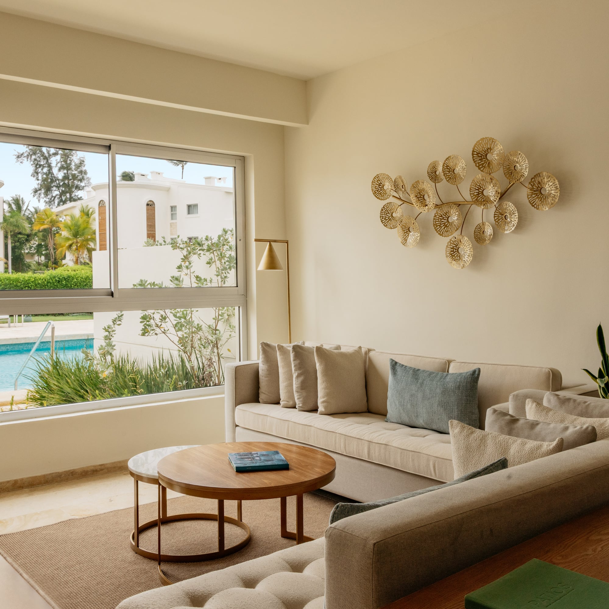 Bright modern living room with beige sofa, gold art, and pool view.