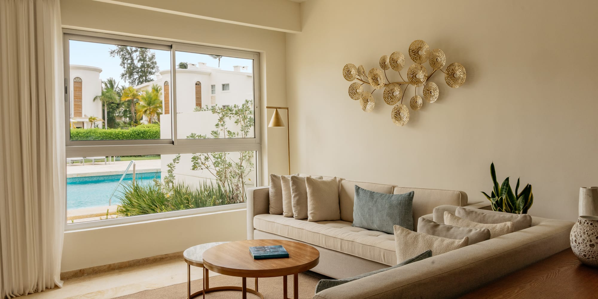 Bright modern living room with beige sofa, gold art, and pool view.