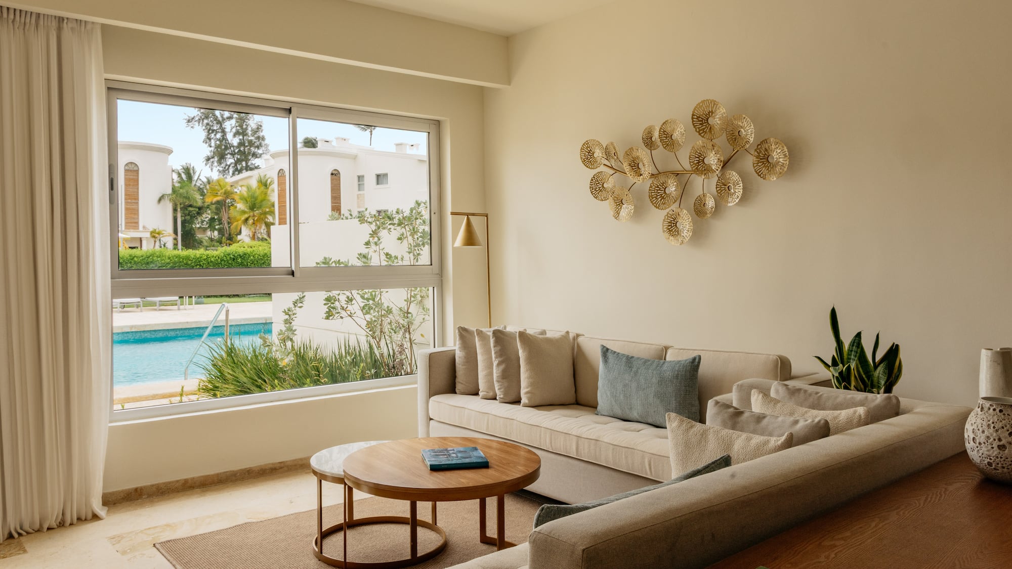 Bright modern living room with beige sofa, gold art, and pool view.