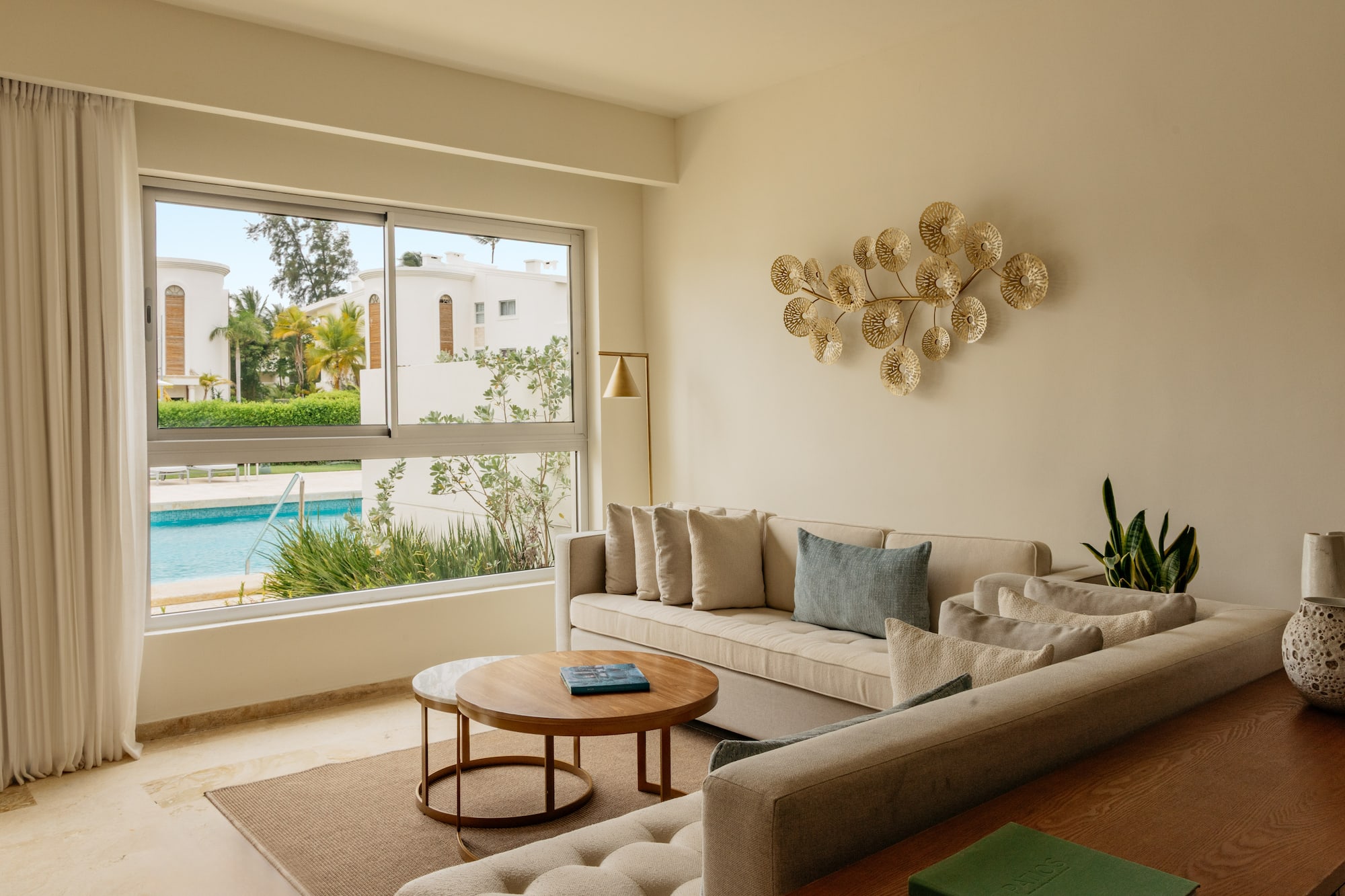 Bright modern living room with beige sofa, gold art, and pool view.
