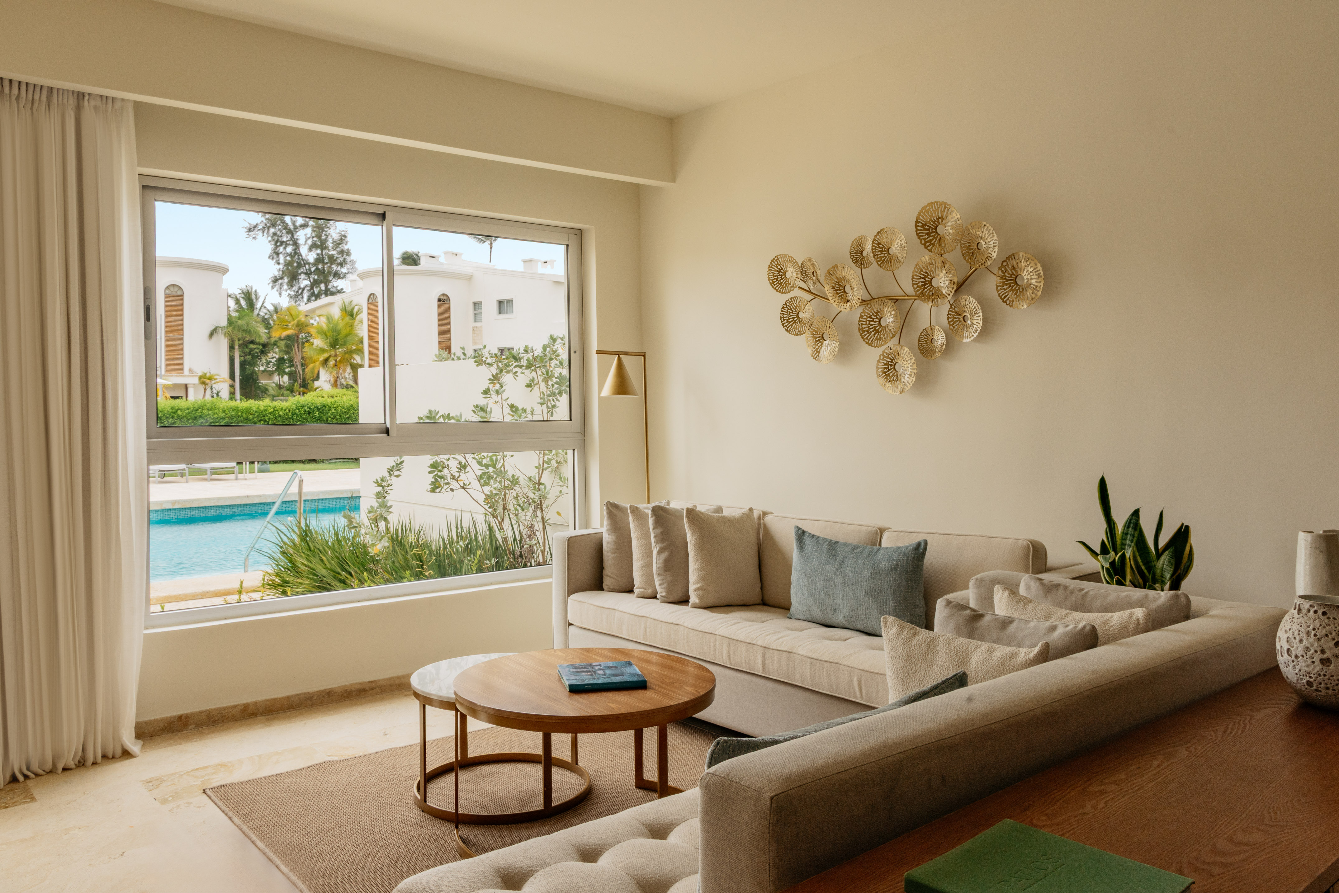 Bright modern living room with beige sofa, gold art, and pool view.