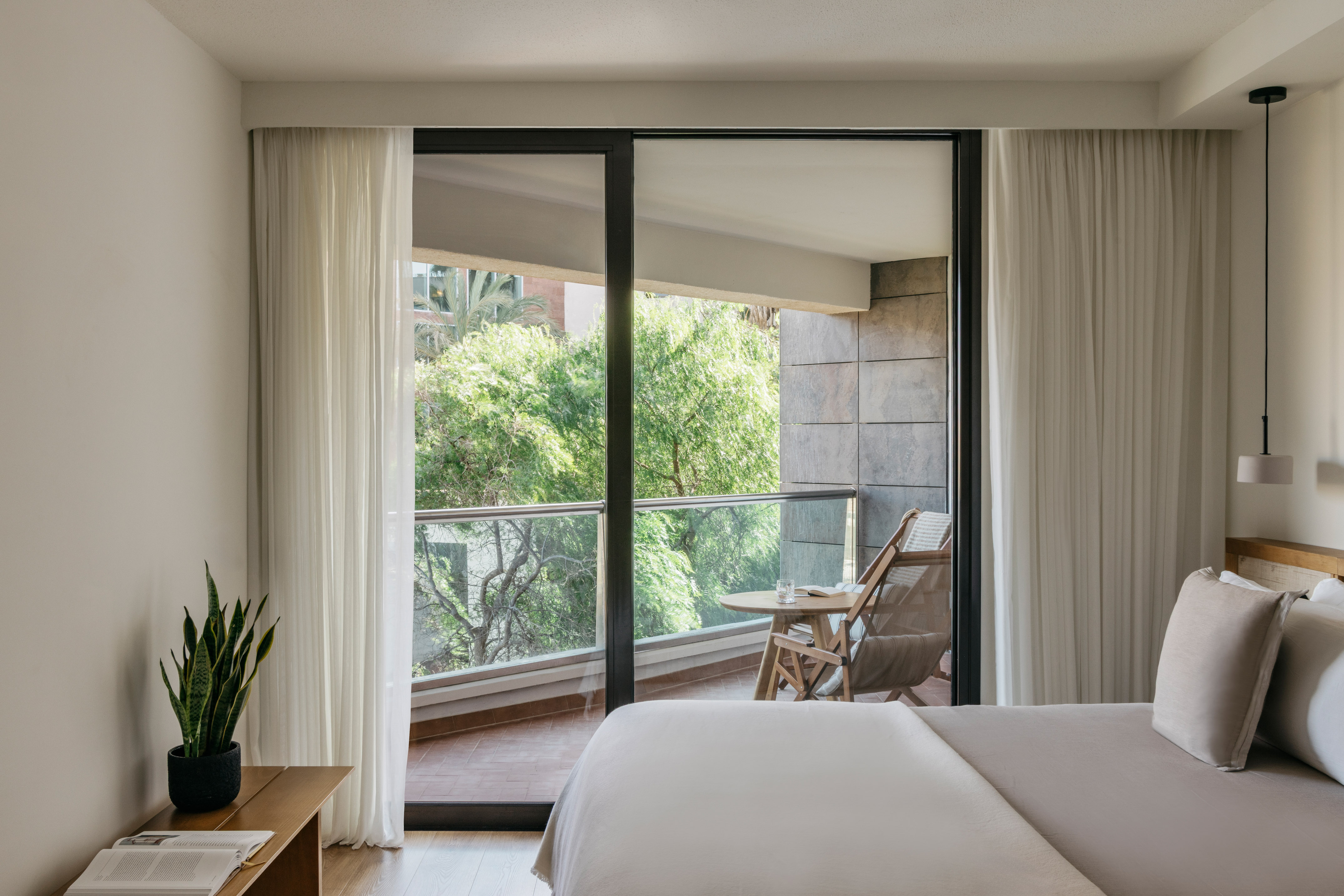 Modern bedroom with private balcony, outdoor seating, and lush green view.
