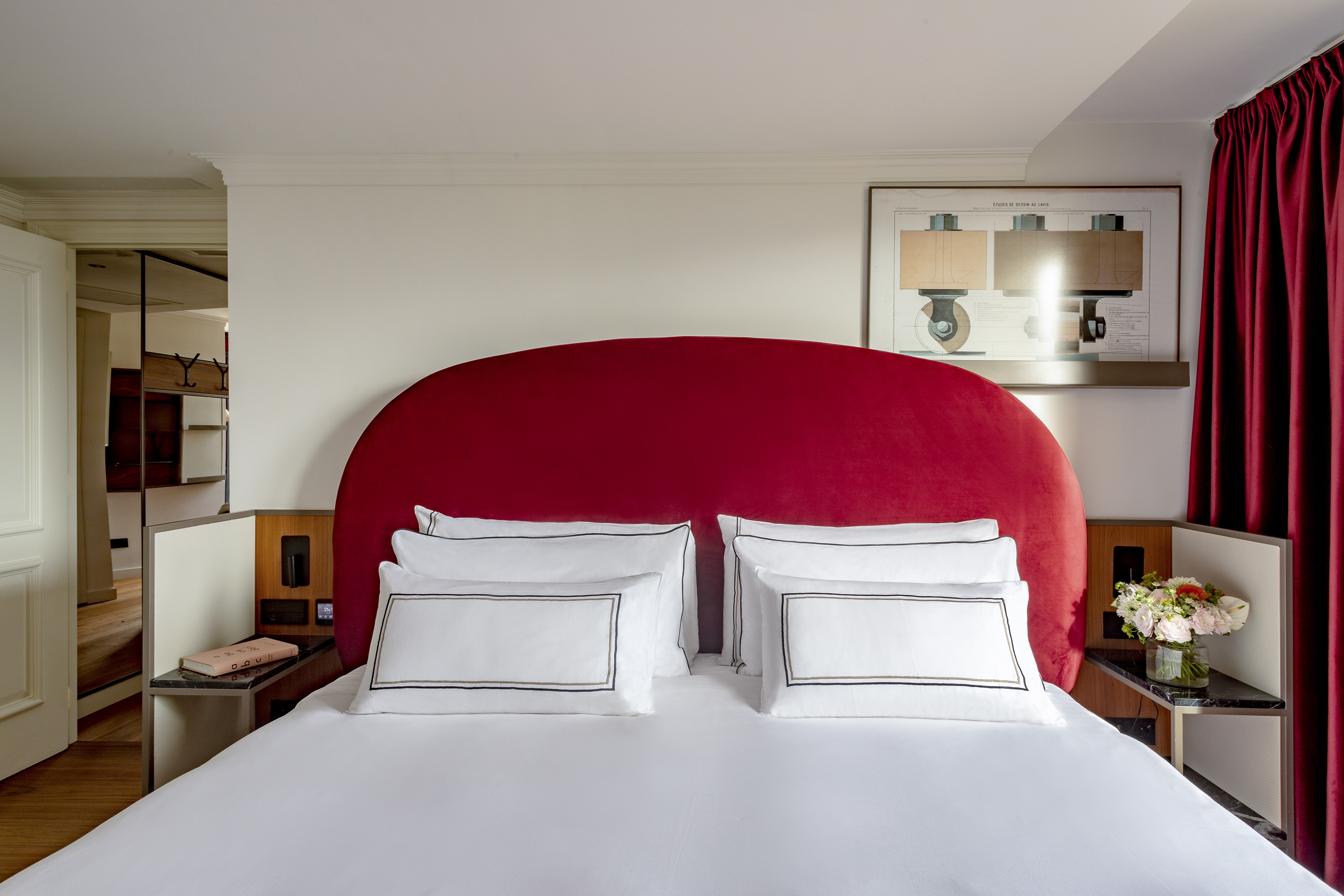 Chic bedroom with red velvet headboard, white bedding, and framed artwork.