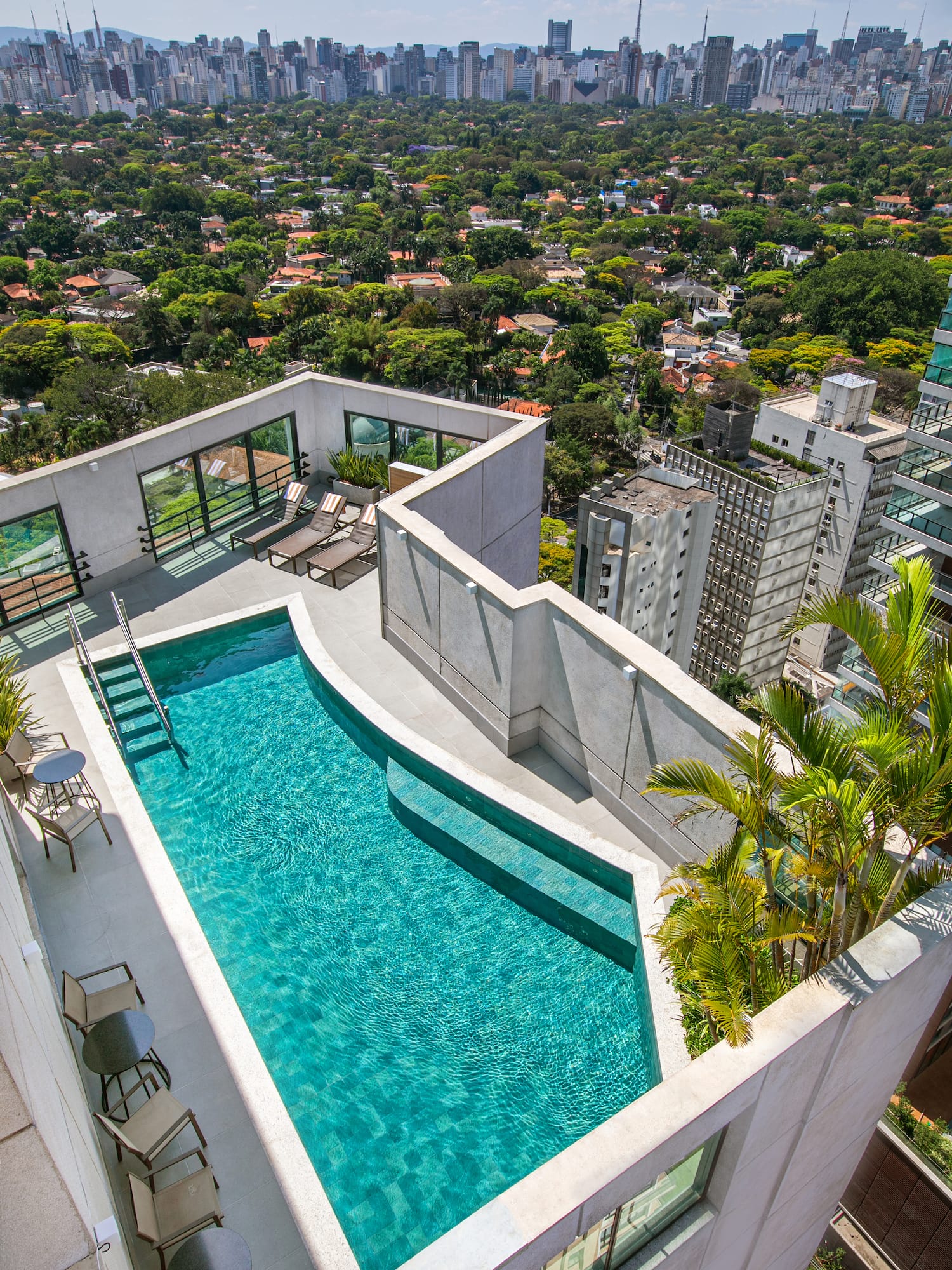 Modern rooftop pool overlooking a green urban city skyline.