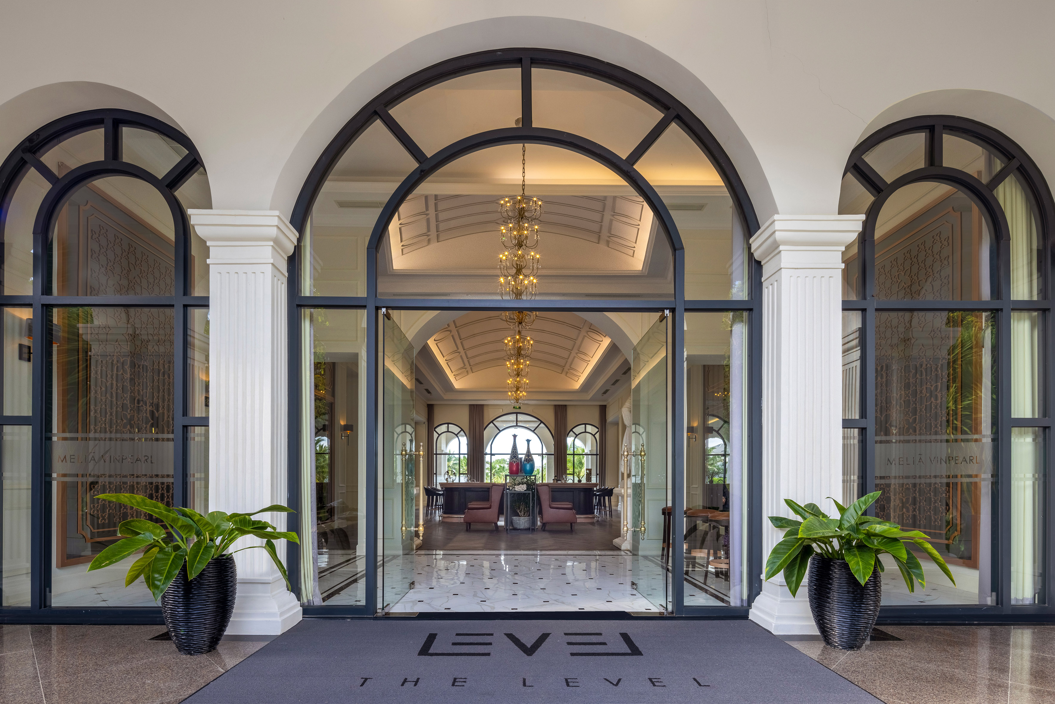 Grand Meliá Vinpearl hotel entrance, arched glass doors, elegant lobby, THE LEVEL mat.