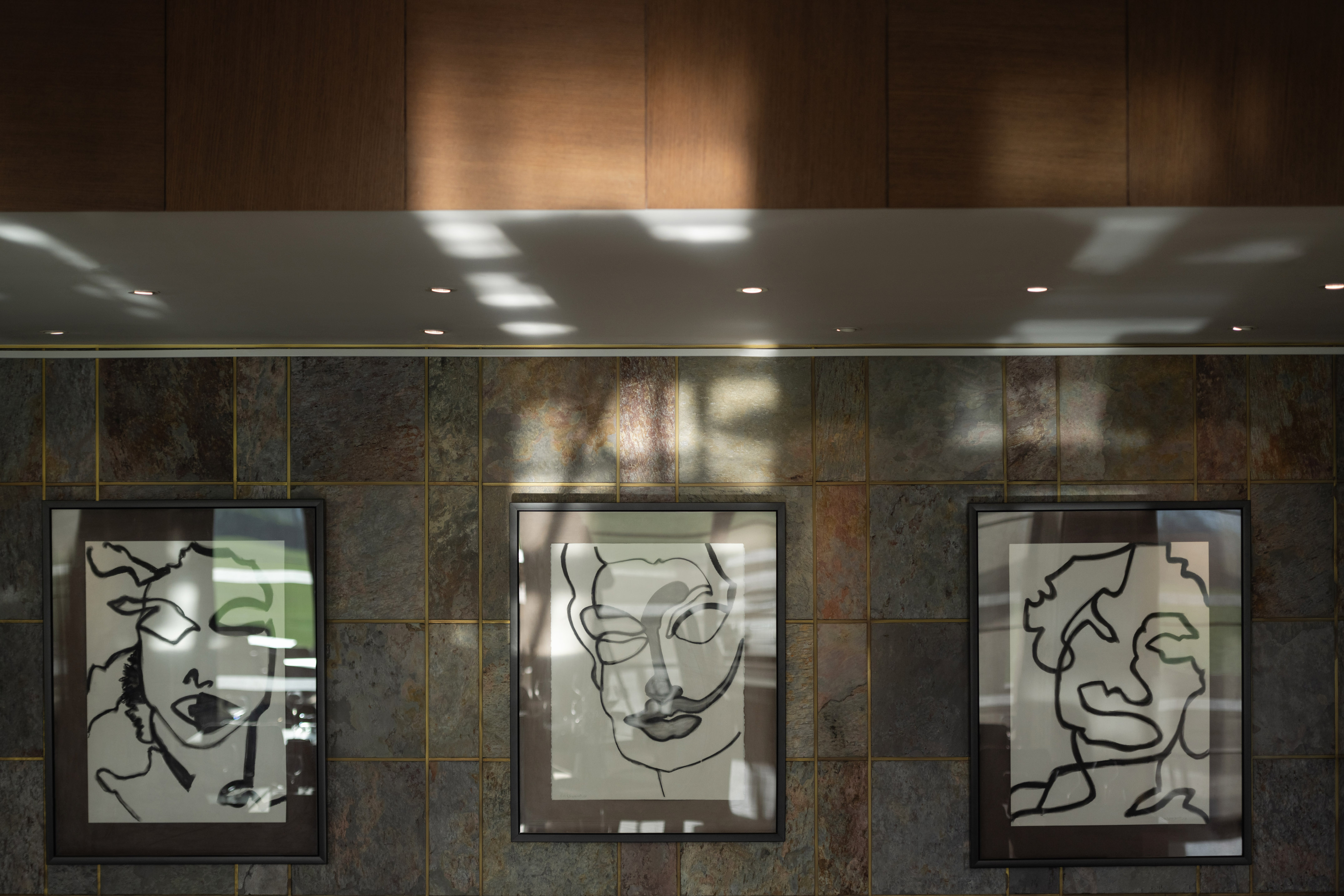 Modern abstract line art faces framed on a dark textured tile wall.