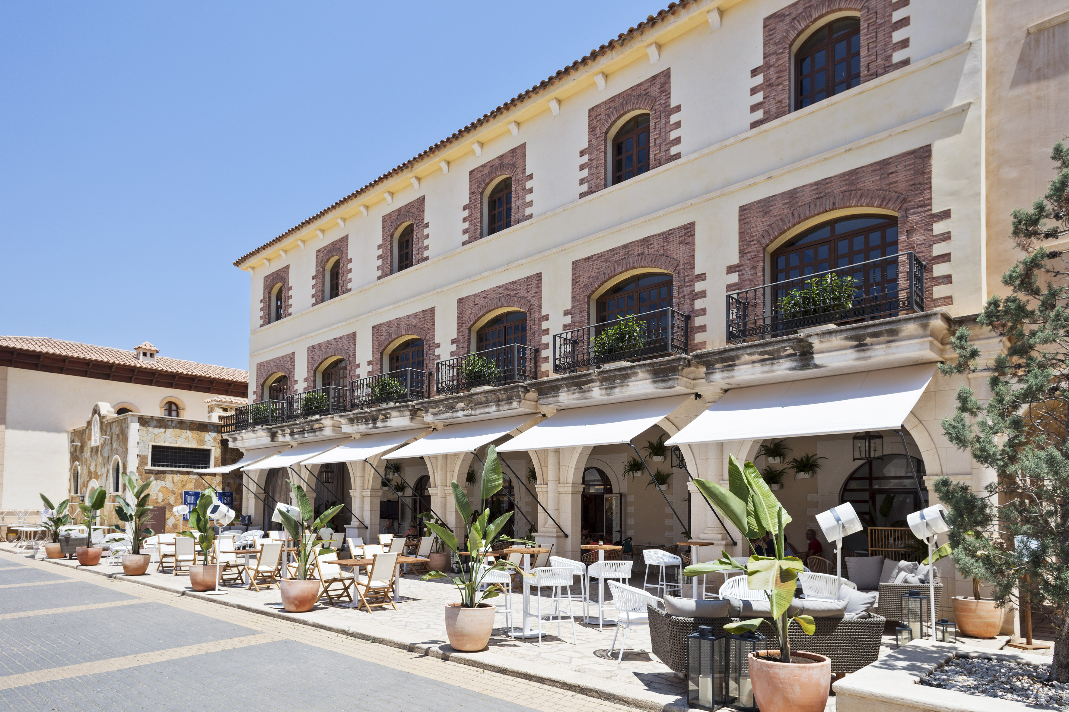Mediterranean building with outdoor cafe, white awnings, and arched windows.