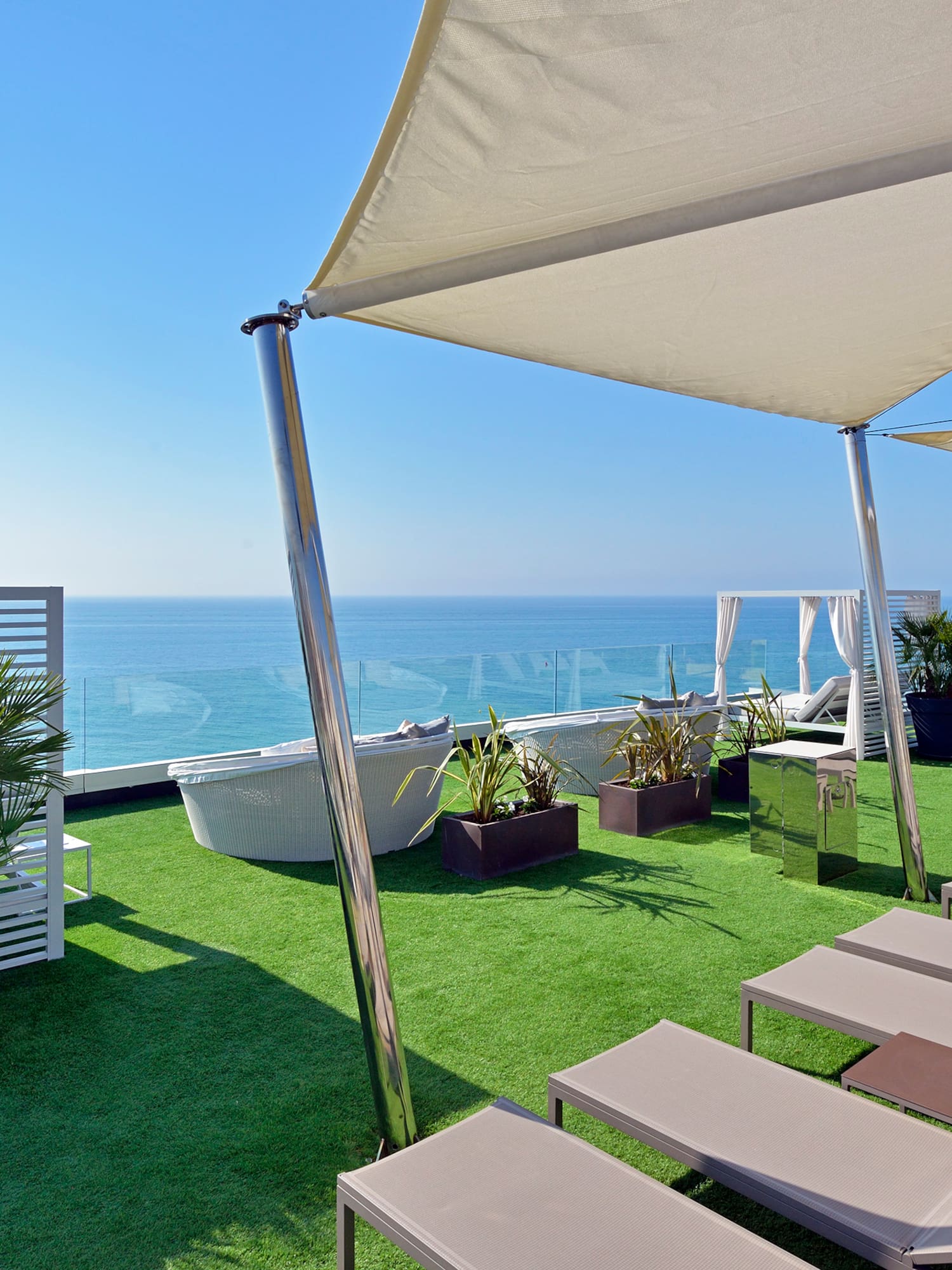 Resort rooftop terrace with ocean view, lounge chairs, and artificial grass.