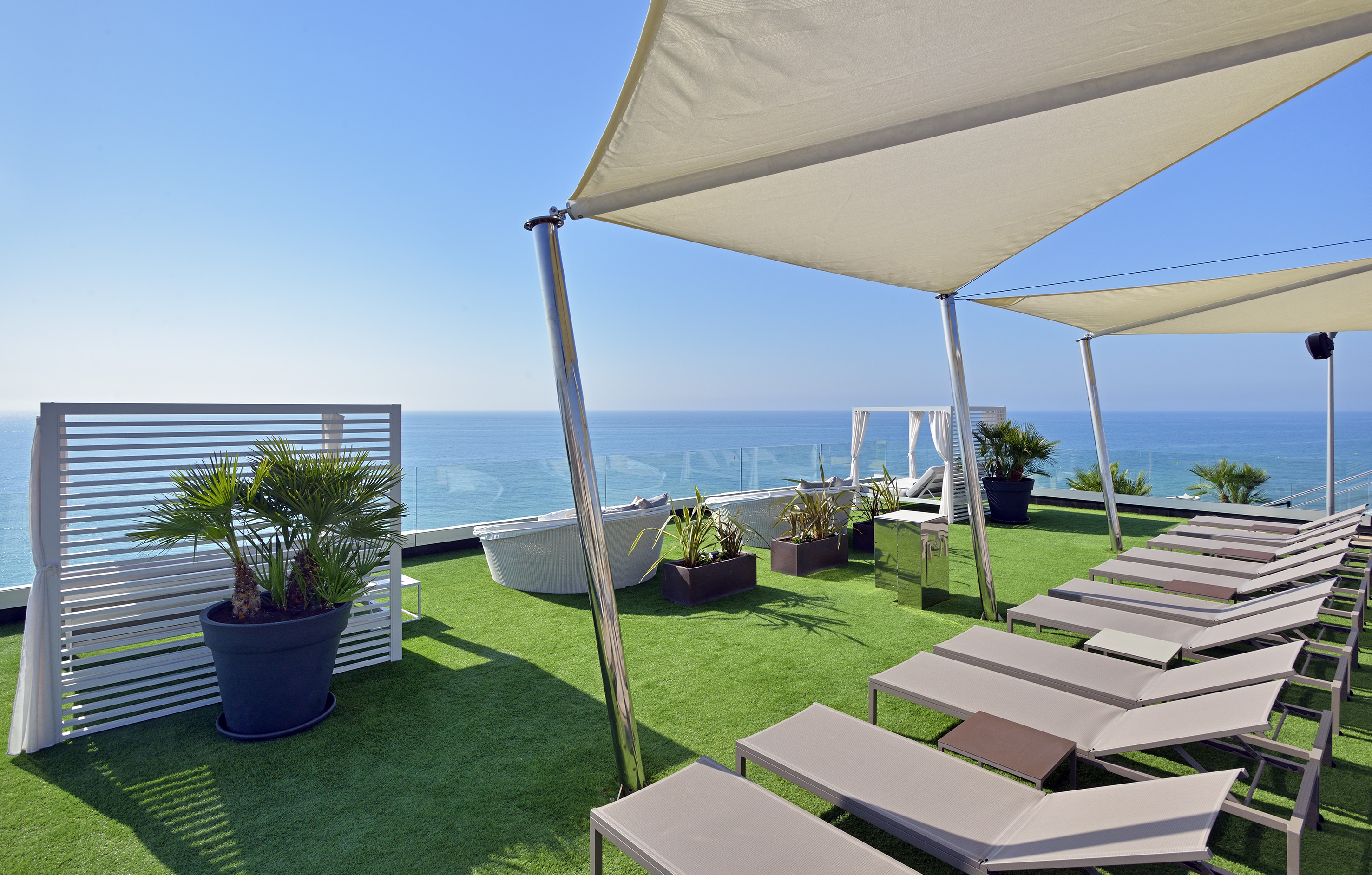Resort rooftop terrace with ocean view, lounge chairs, and artificial grass.