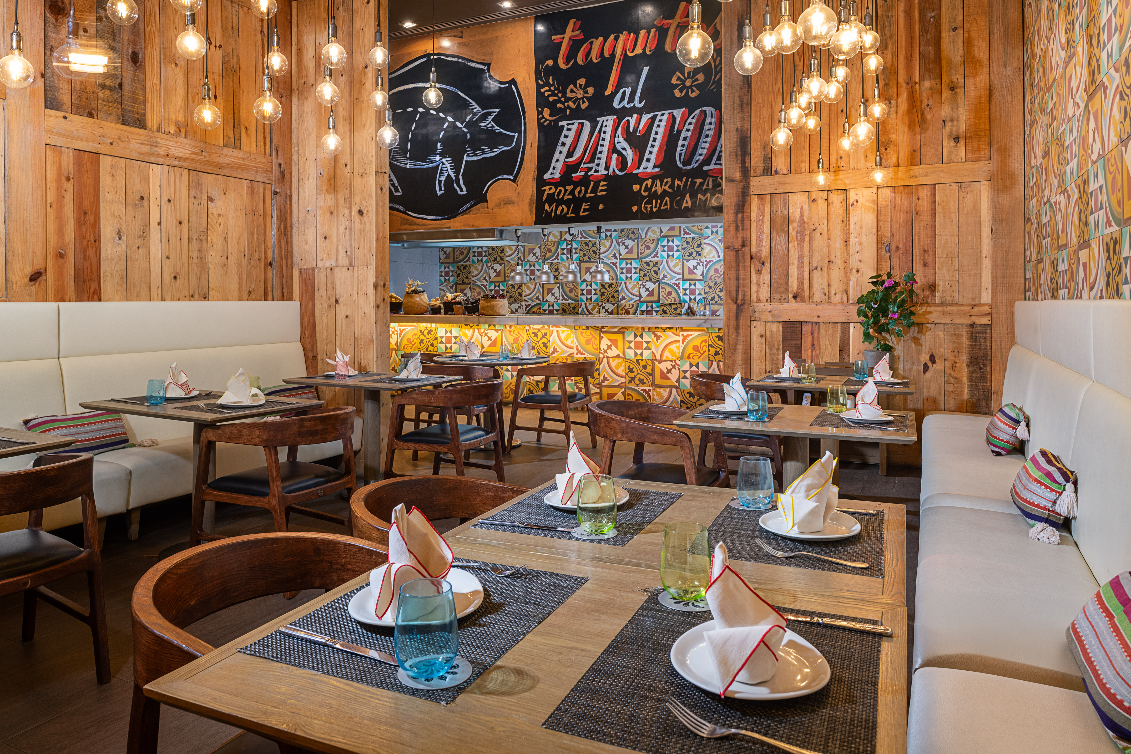 Mexican restaurant interior with wood paneling, Edison lights, colorful tiled bar.
