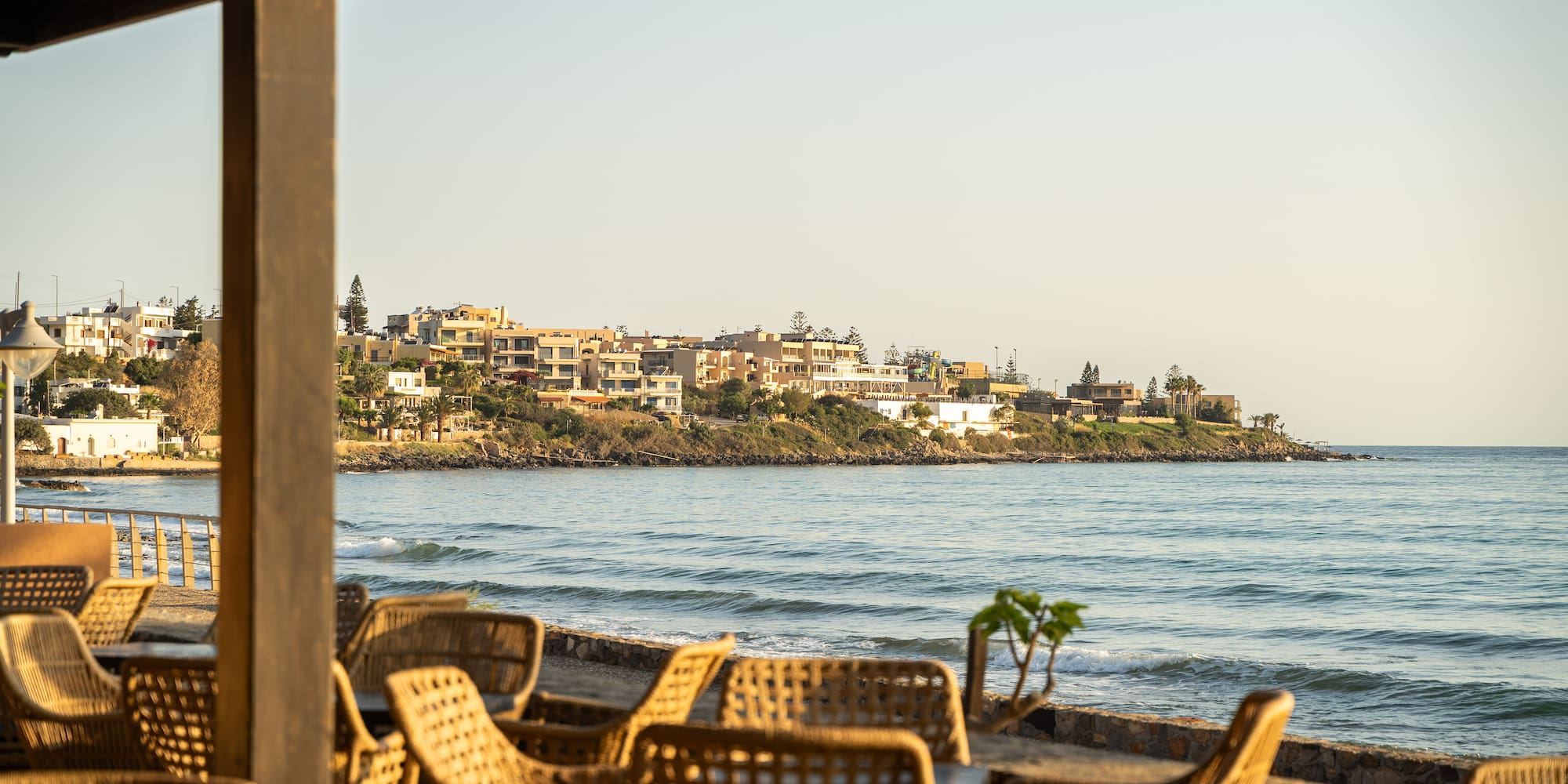 Coastal restaurant patio with wicker chairs facing the ocean and resort town.
