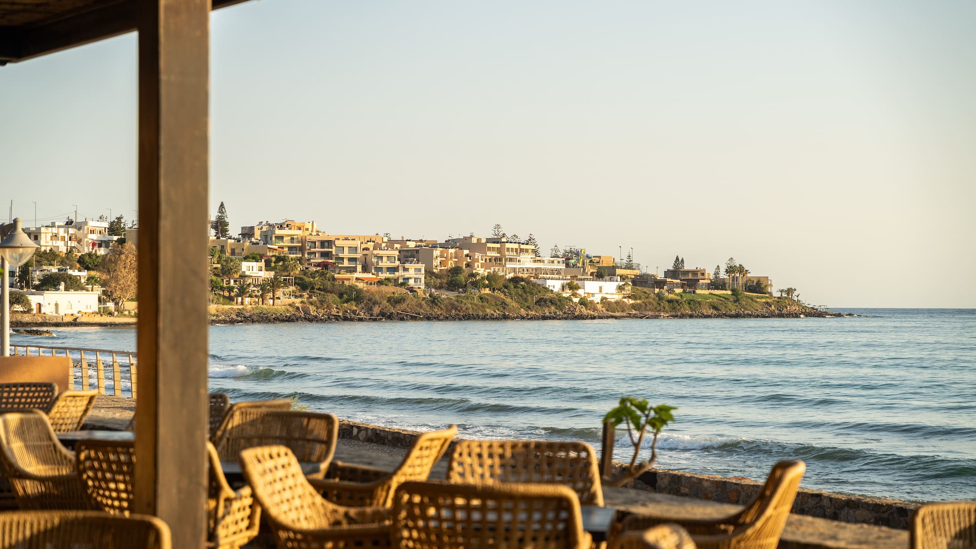 Coastal restaurant patio with wicker chairs facing the ocean and resort town.