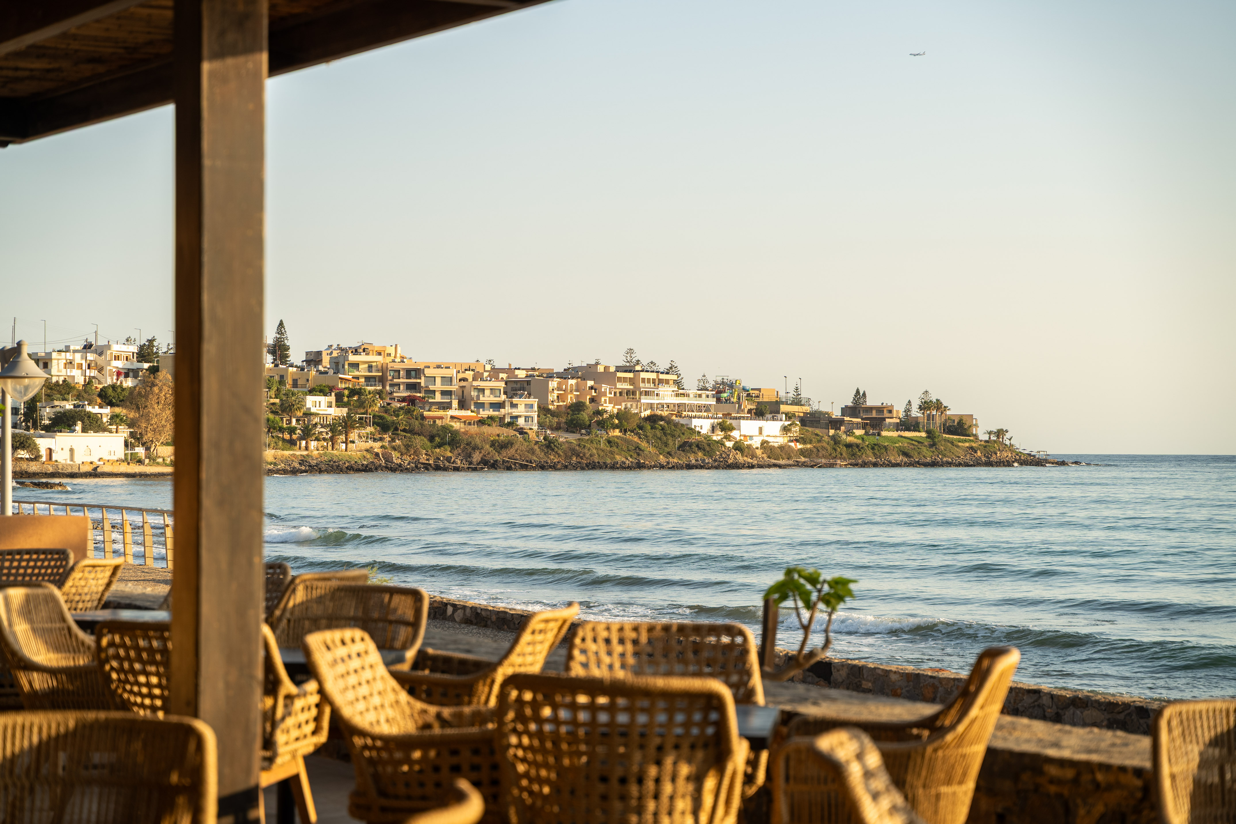 Coastal restaurant patio with wicker chairs facing the ocean and resort town.