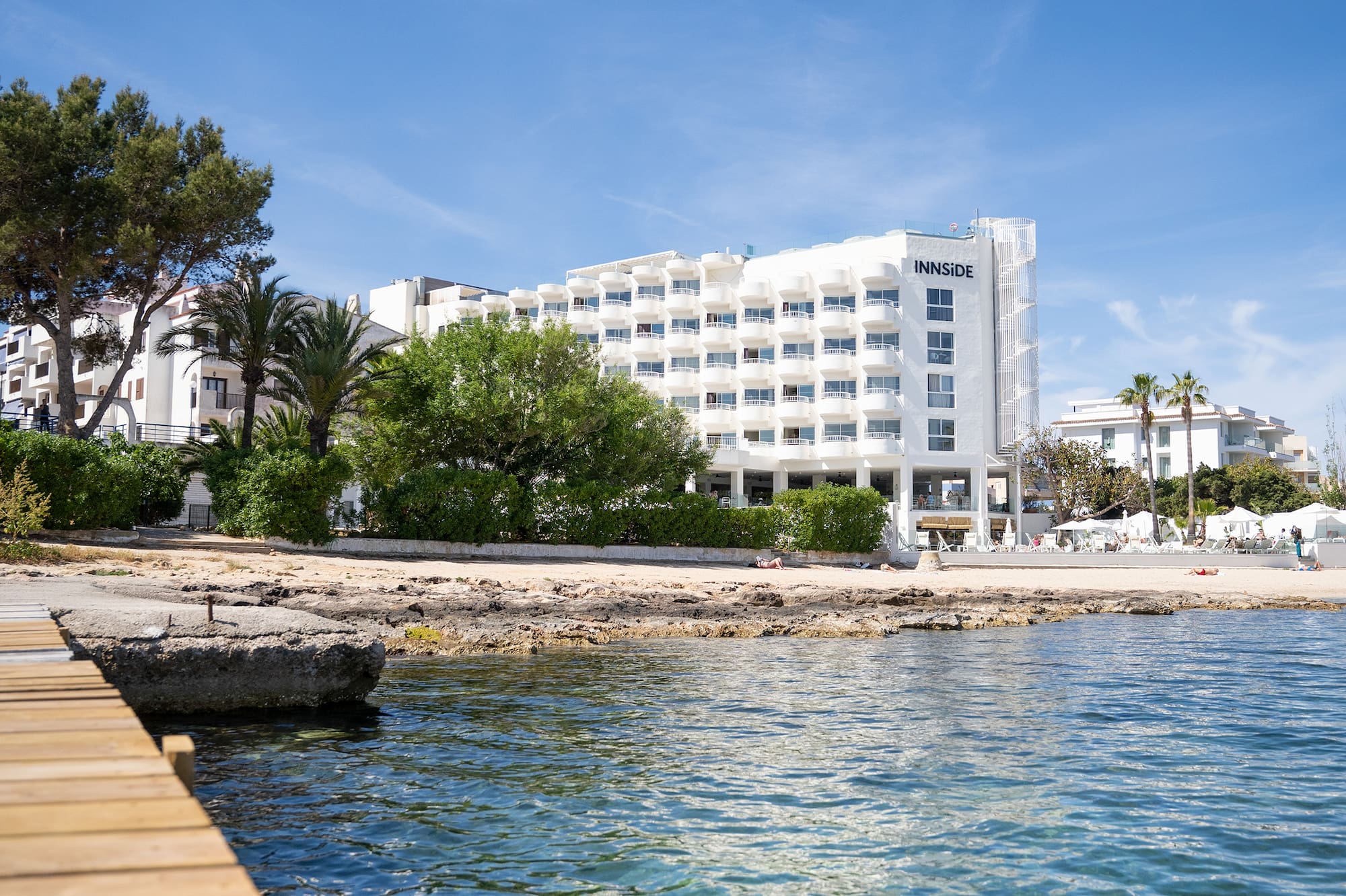 Coastal INNSIDE hotel, sunny beach, clear blue sea, and wooden pier.