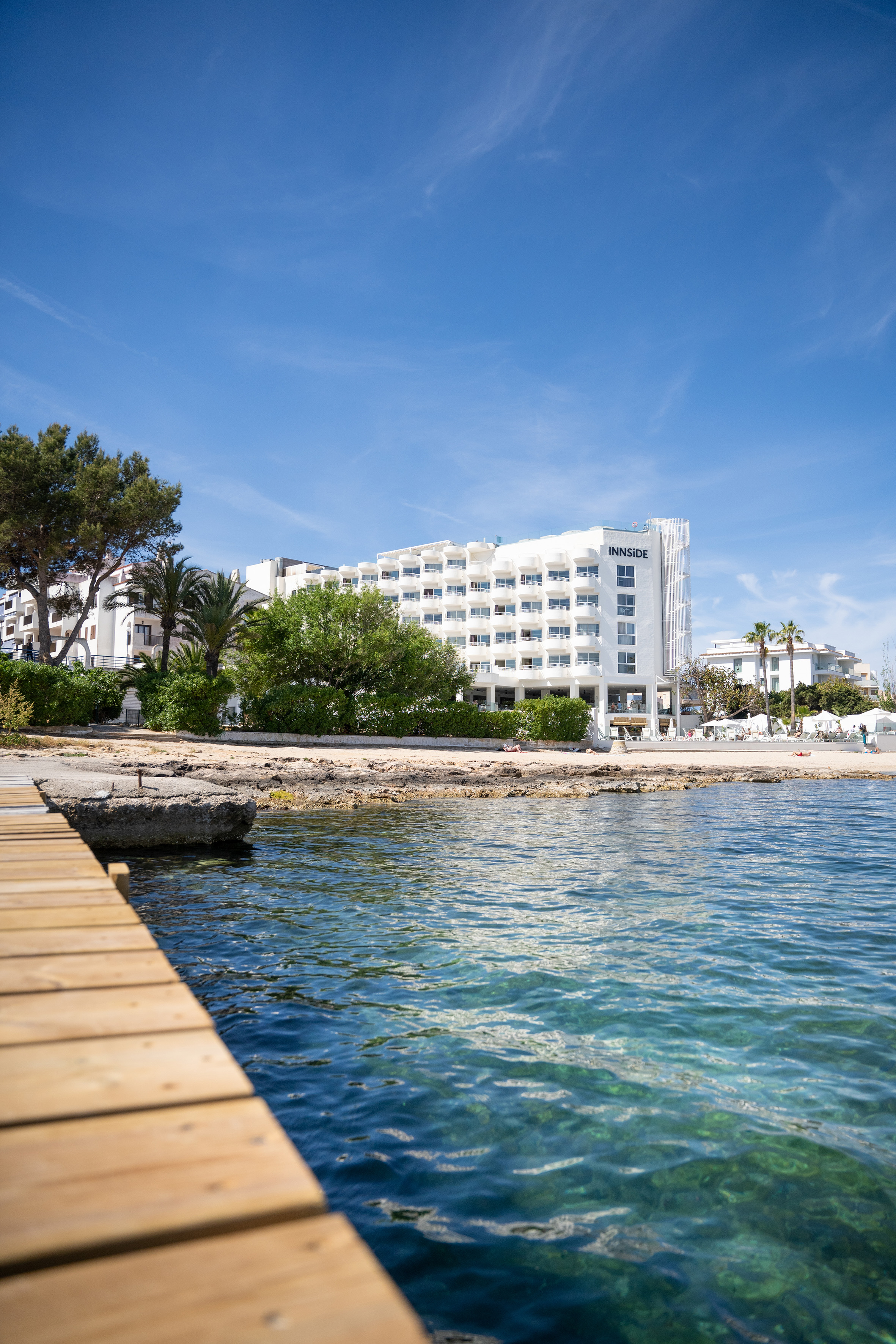 Coastal INNSIDE hotel, sunny beach, clear blue sea, and wooden pier.