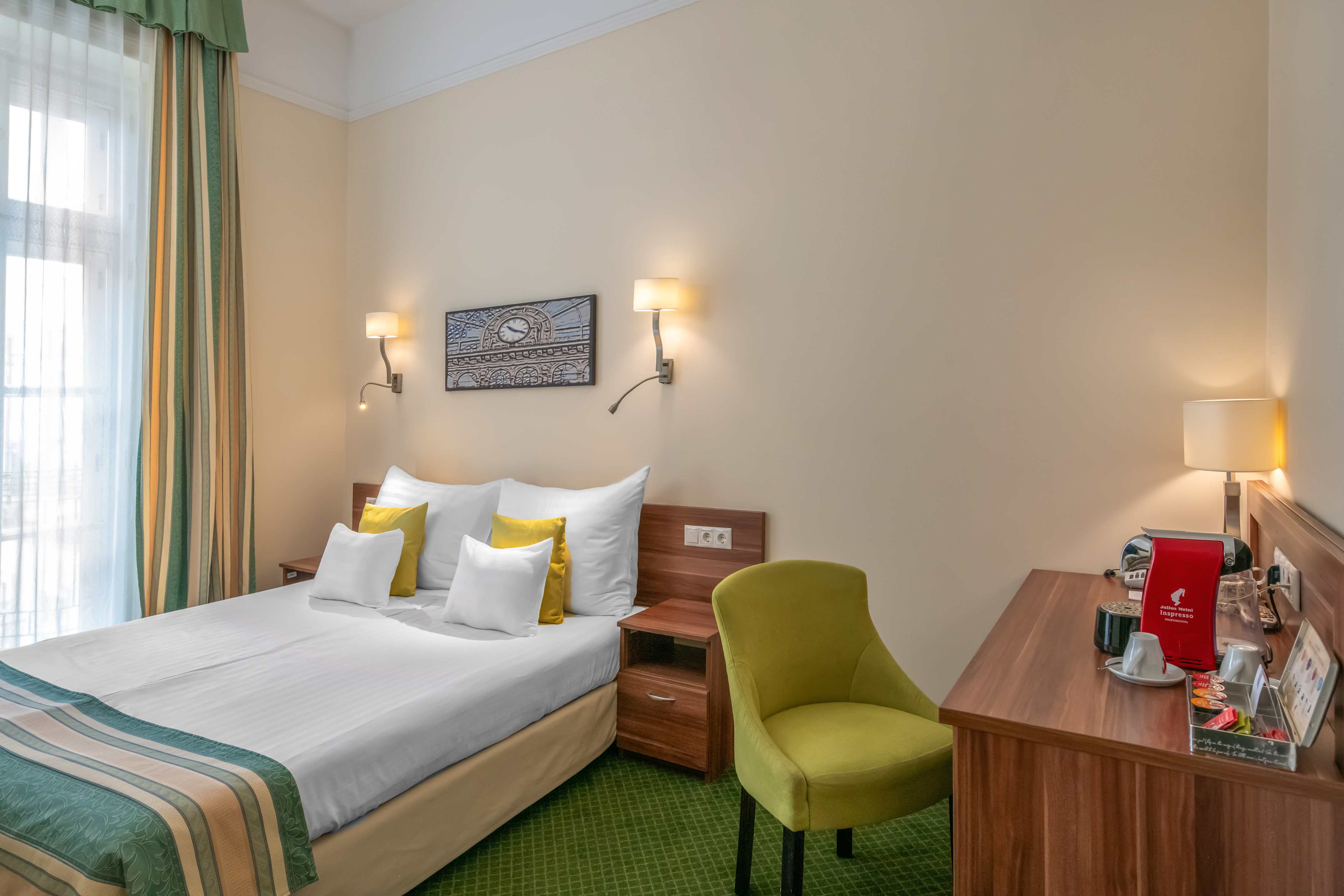 Hotel room with double bed, green carpet, coffee station, and window.