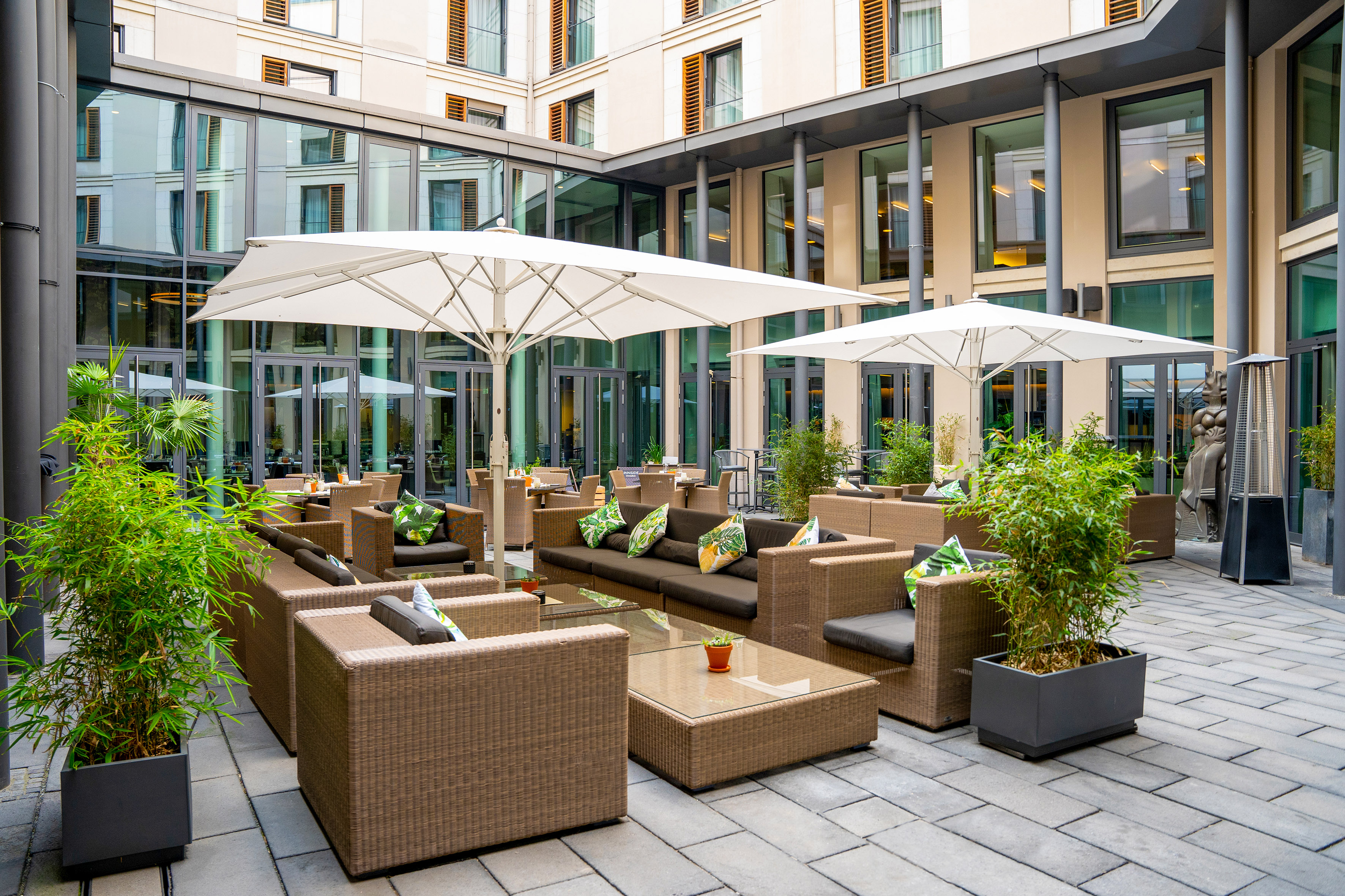 Modern hotel courtyard with outdoor lounge seating, white umbrellas, and plants.